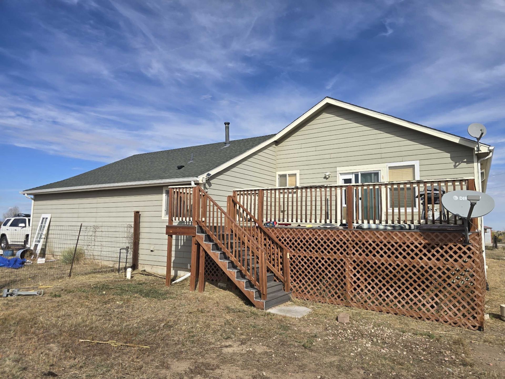 Suburban house with wooden deck and stairs, beige siding, and a satellite dish under a blue sky