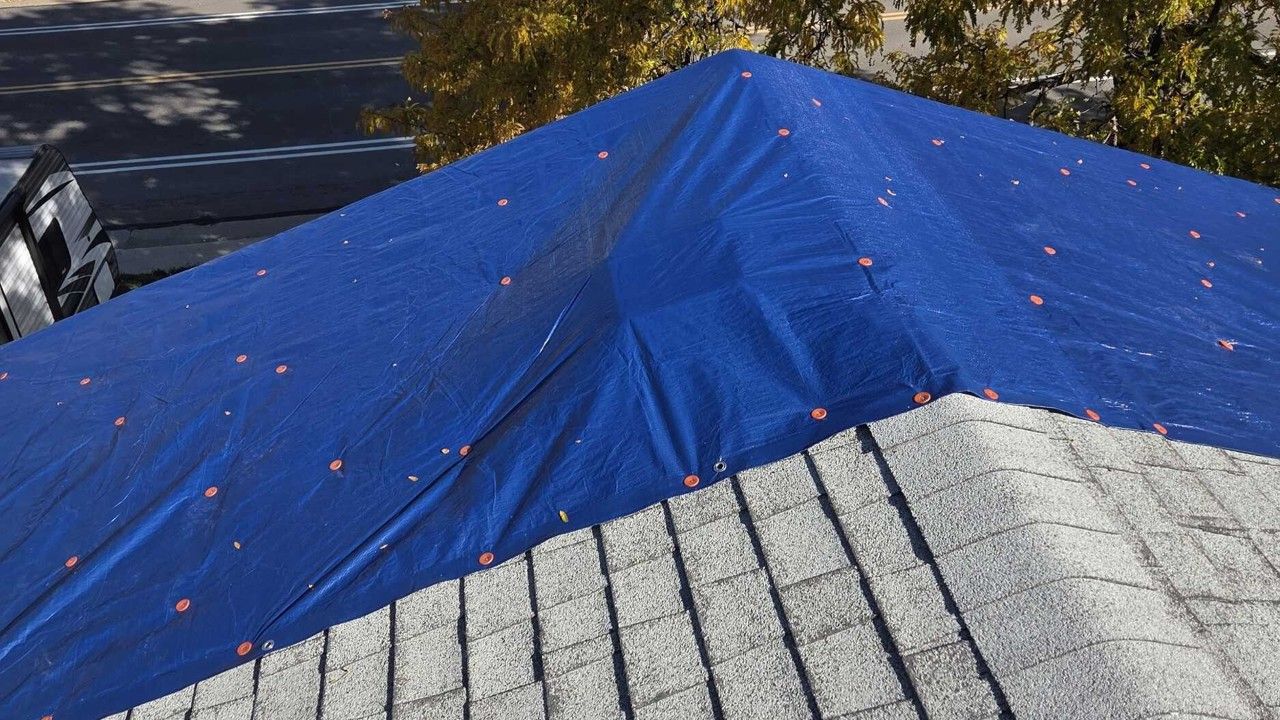 Blue tarp covering part of a gray shingled roof in sunlight