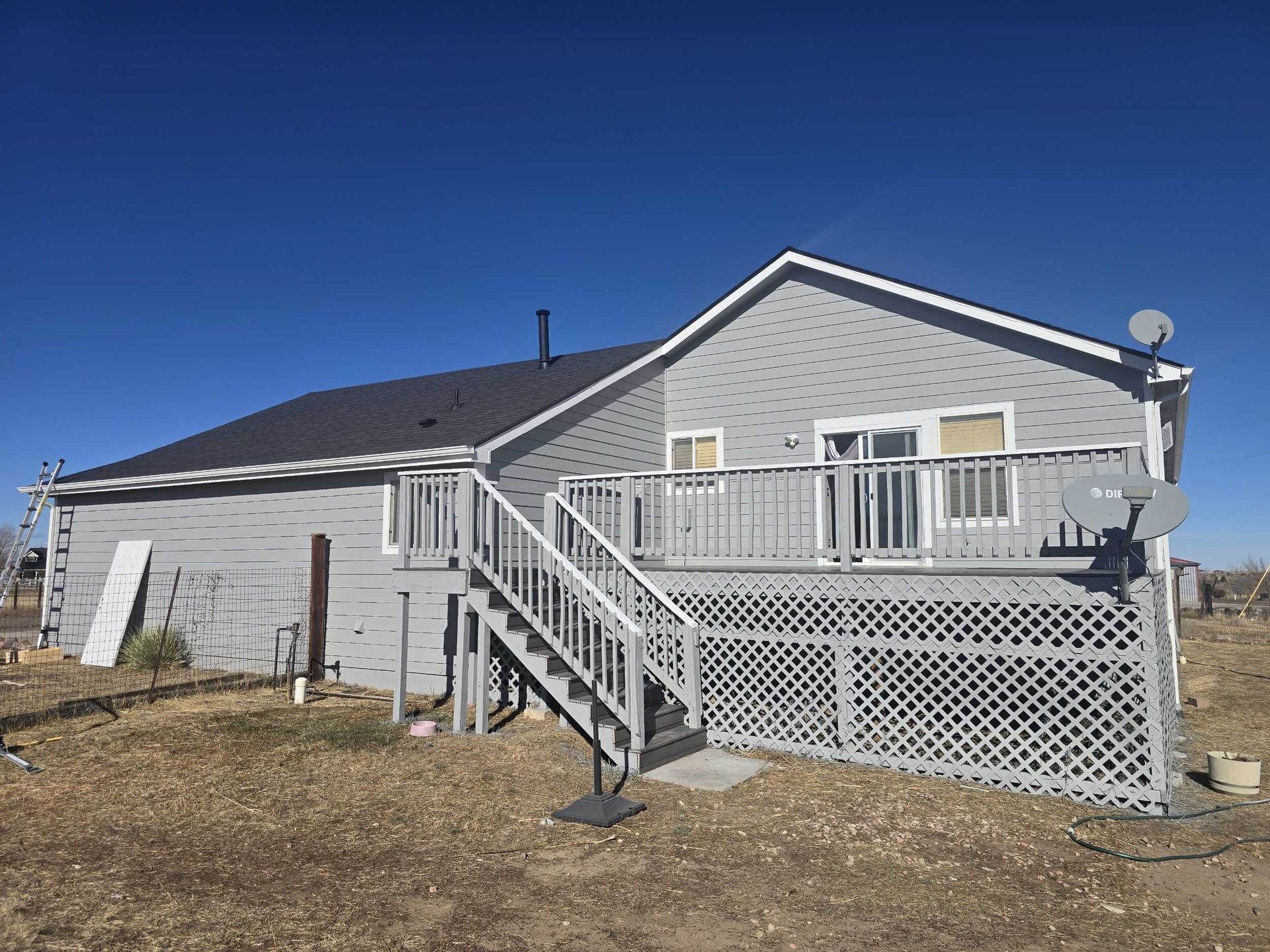 Gray house with white deck and stairs on a sunny day under a clear blue sky