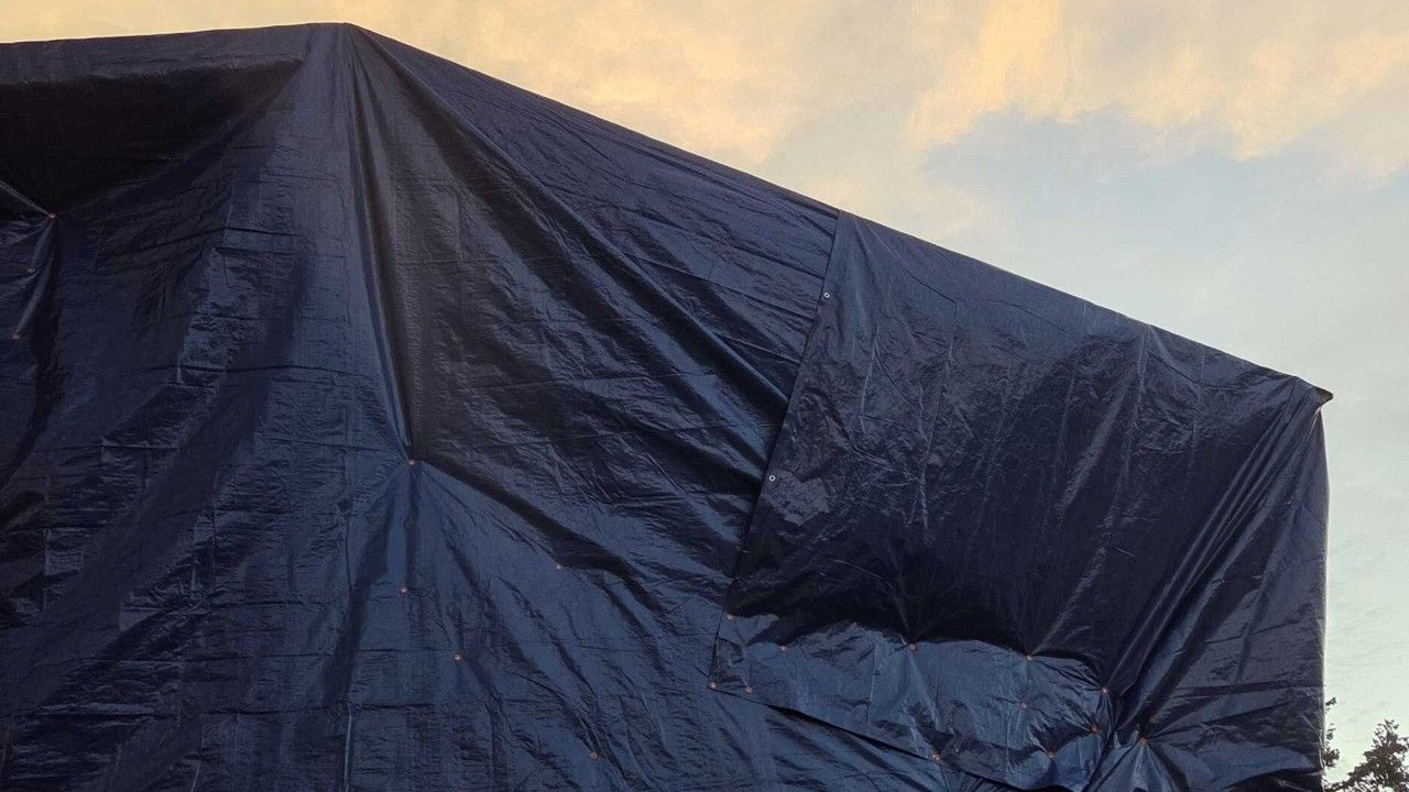 Large dark blue tarp draped over a structure outdoors against a cloudy sky