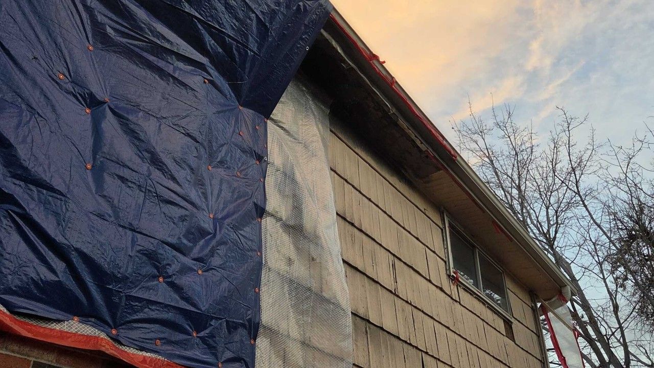 Blue tarp covering an unfinished brick wall beside a roofline at sunset