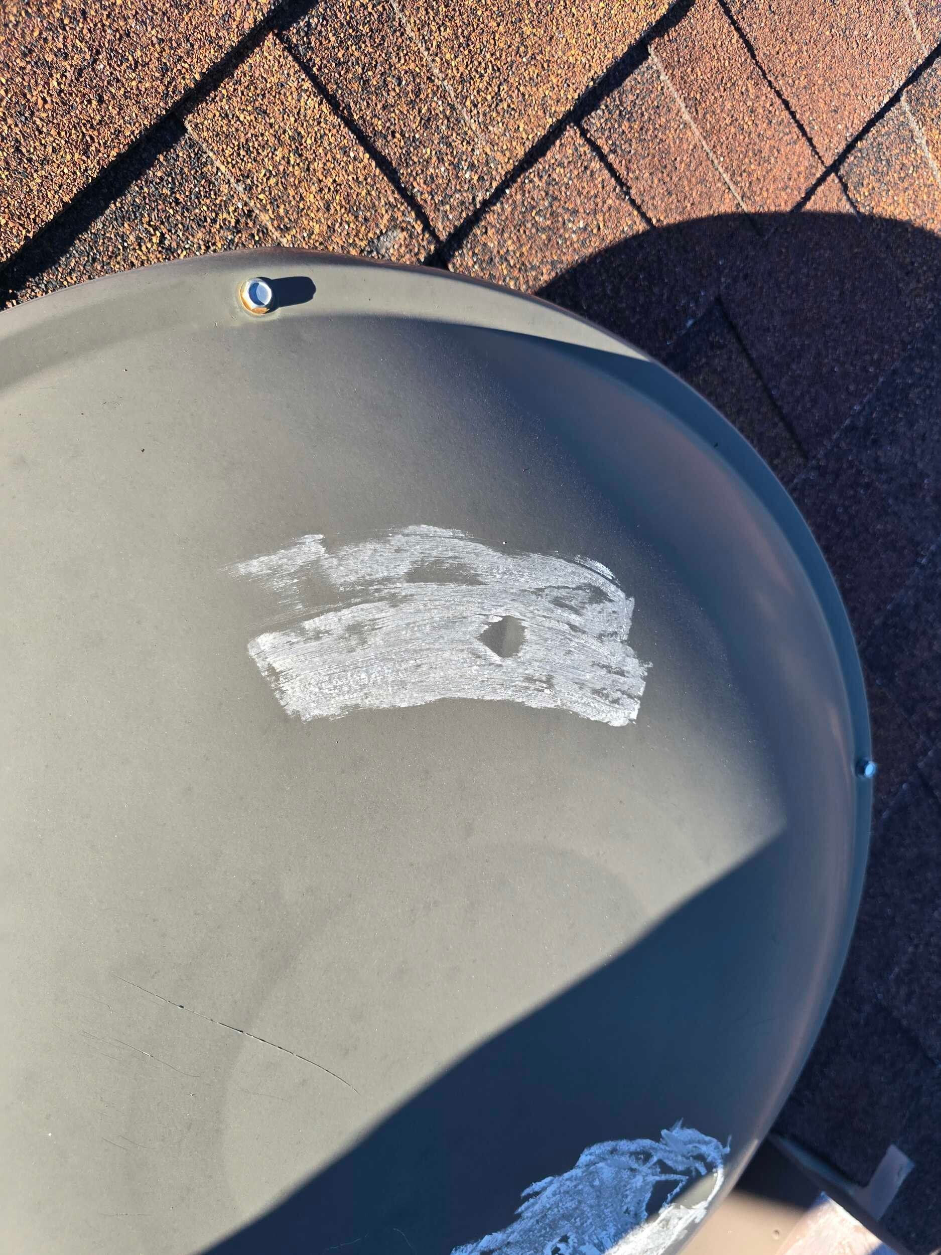 Gray grill lid with white paint scratches on a sunlit tiled patio