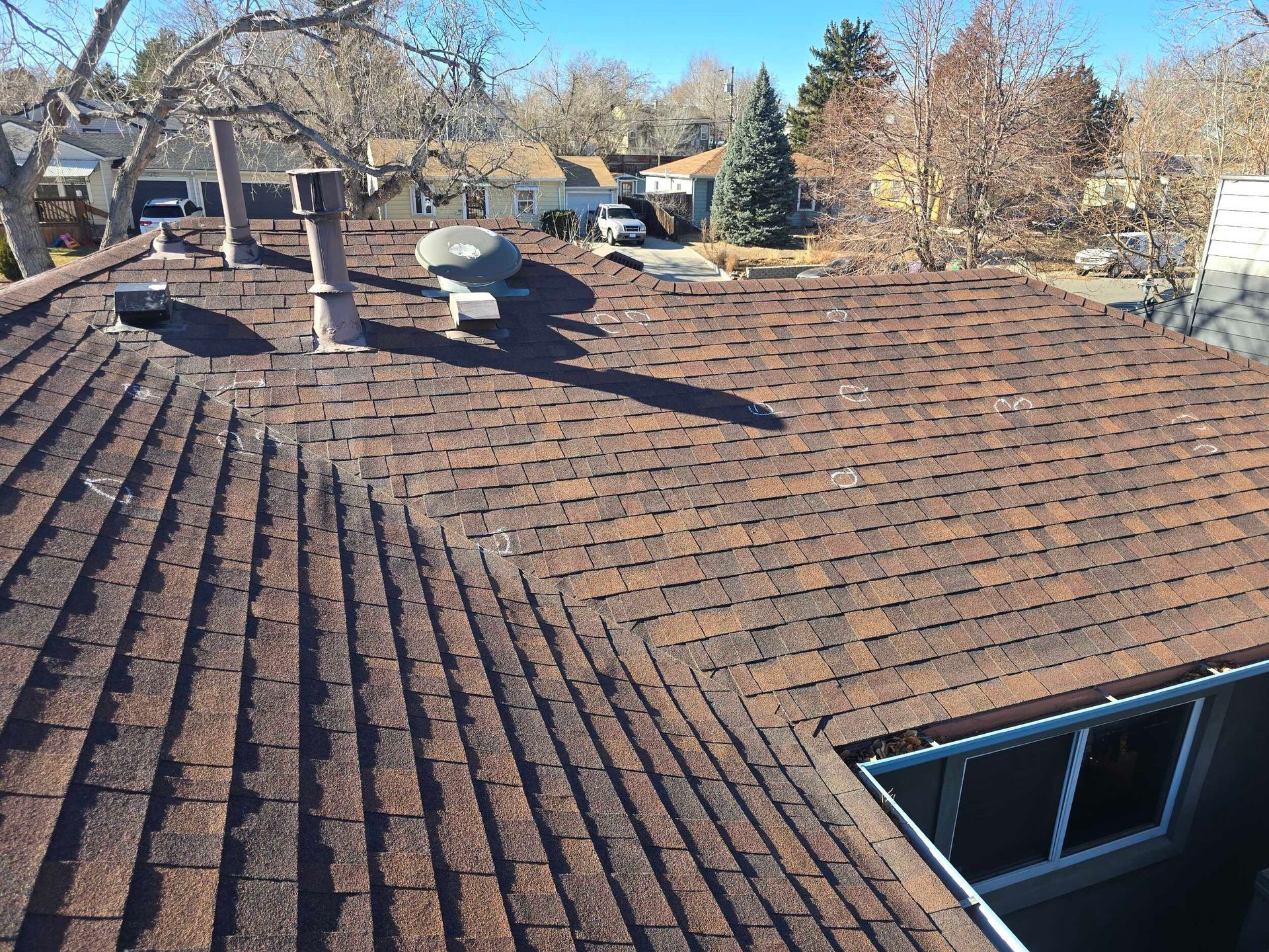 Rooftop with brown shingle tiles, skylight, and vents under a clear sky