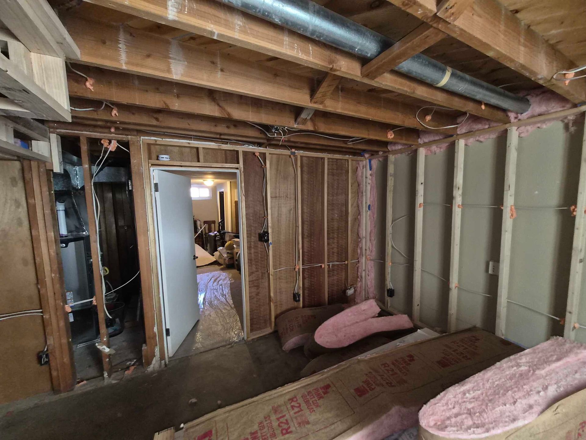 Partially finished basement with exposed studs, insulation, and ceiling beams, viewed through a doorway