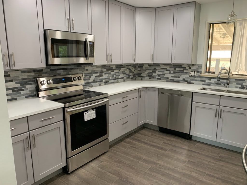 Modern gray kitchen with stainless steel appliances, white cabinets, and a tiled backsplash