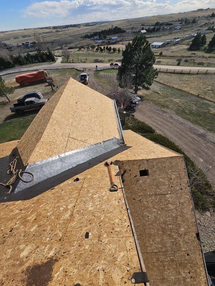 Roof under construction with plywood sheathing overlooking a rural landscape and driveway