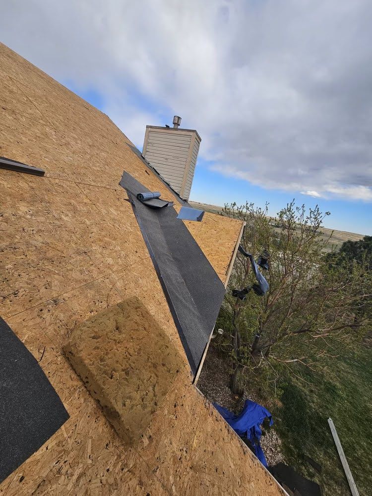 Roof under construction with plywood, black underlayment, and a chimney against a cloudy sky