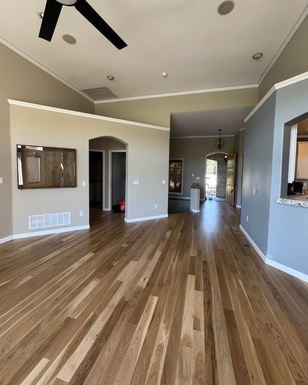 Empty living room with wood floors, gray walls, vaulted ceiling, and ceiling fan.