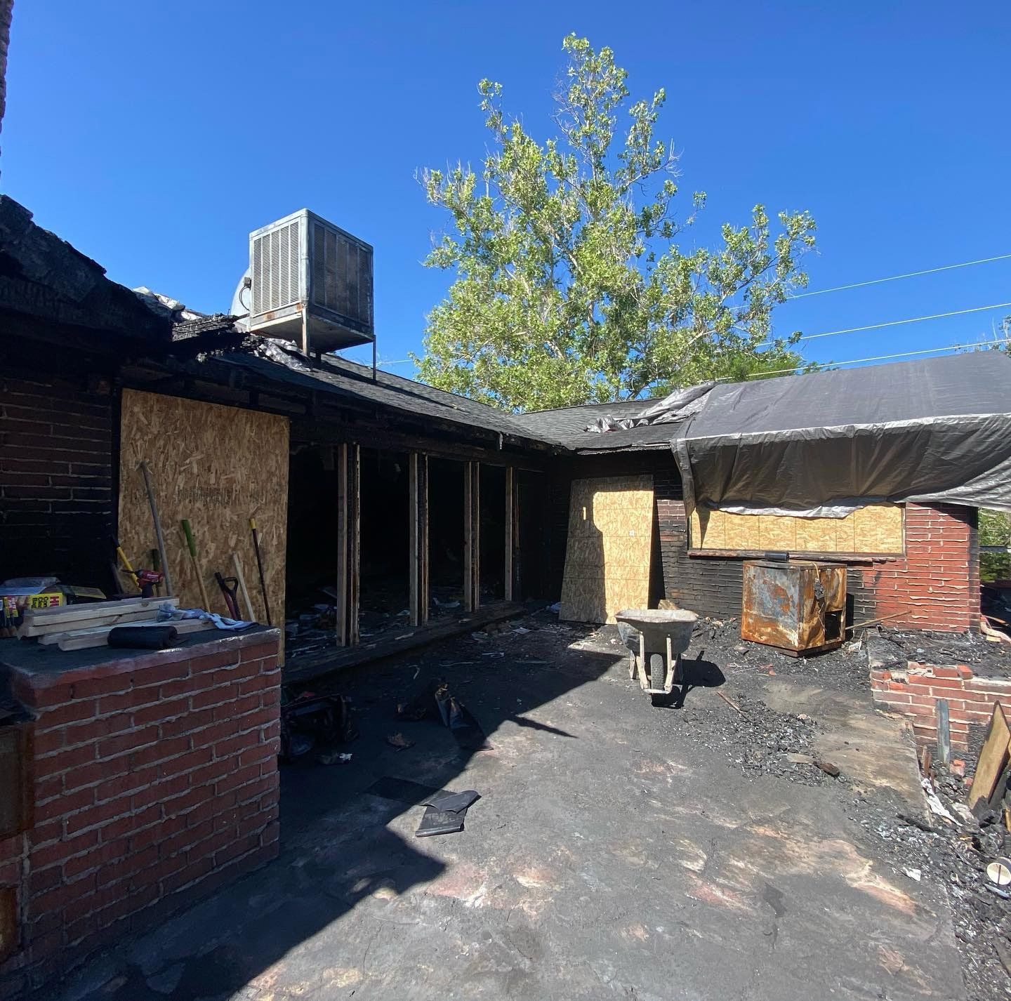 Burned-out backyard patio with charred roof, brick walls, and debris under a bright blue sky