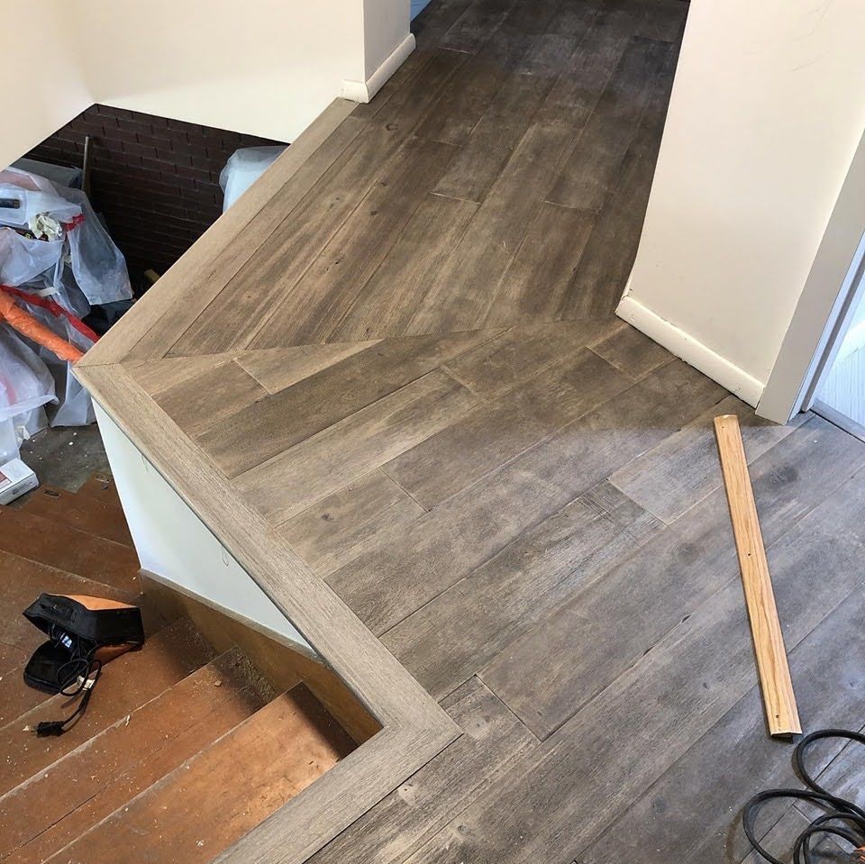 Partially installed gray wood flooring in a hallway, with tools and materials on the floor