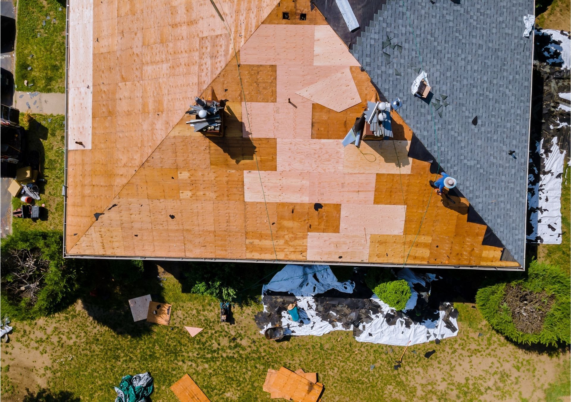Aerial view of workers repairing a roof with orange underlayment and gray shingles, tools and materials below