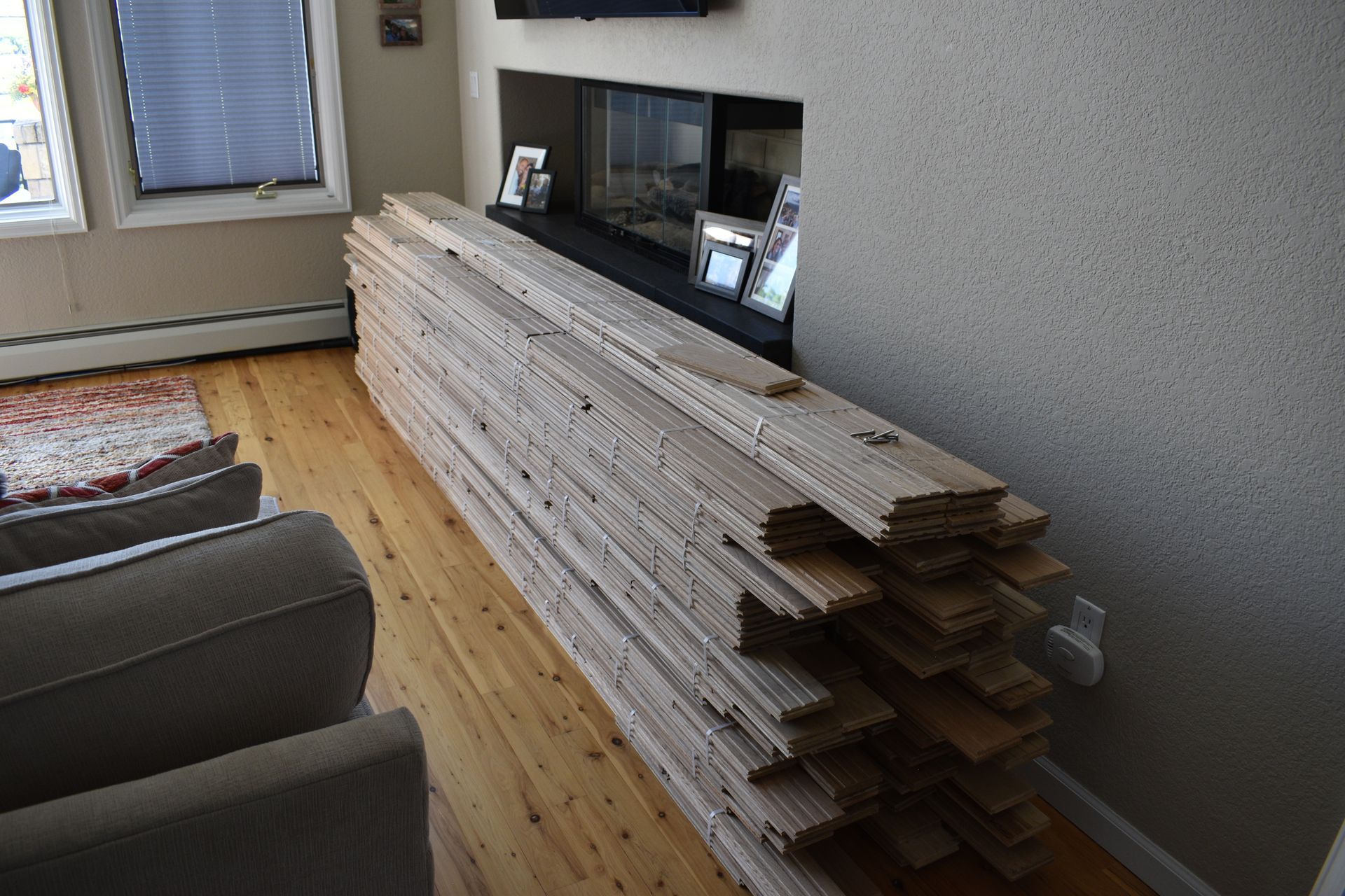Stacked hardwood flooring planks beside a wall in a bright room with a window and radiator.