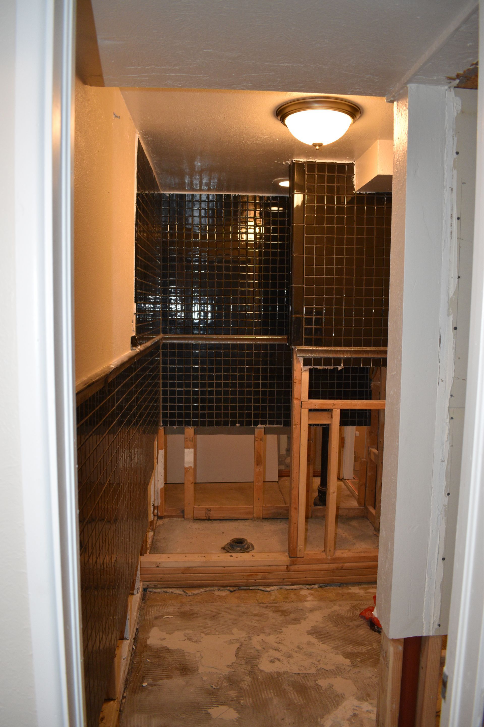 Narrow hallway under construction with exposed framing, wiring, and a bare light fixture.