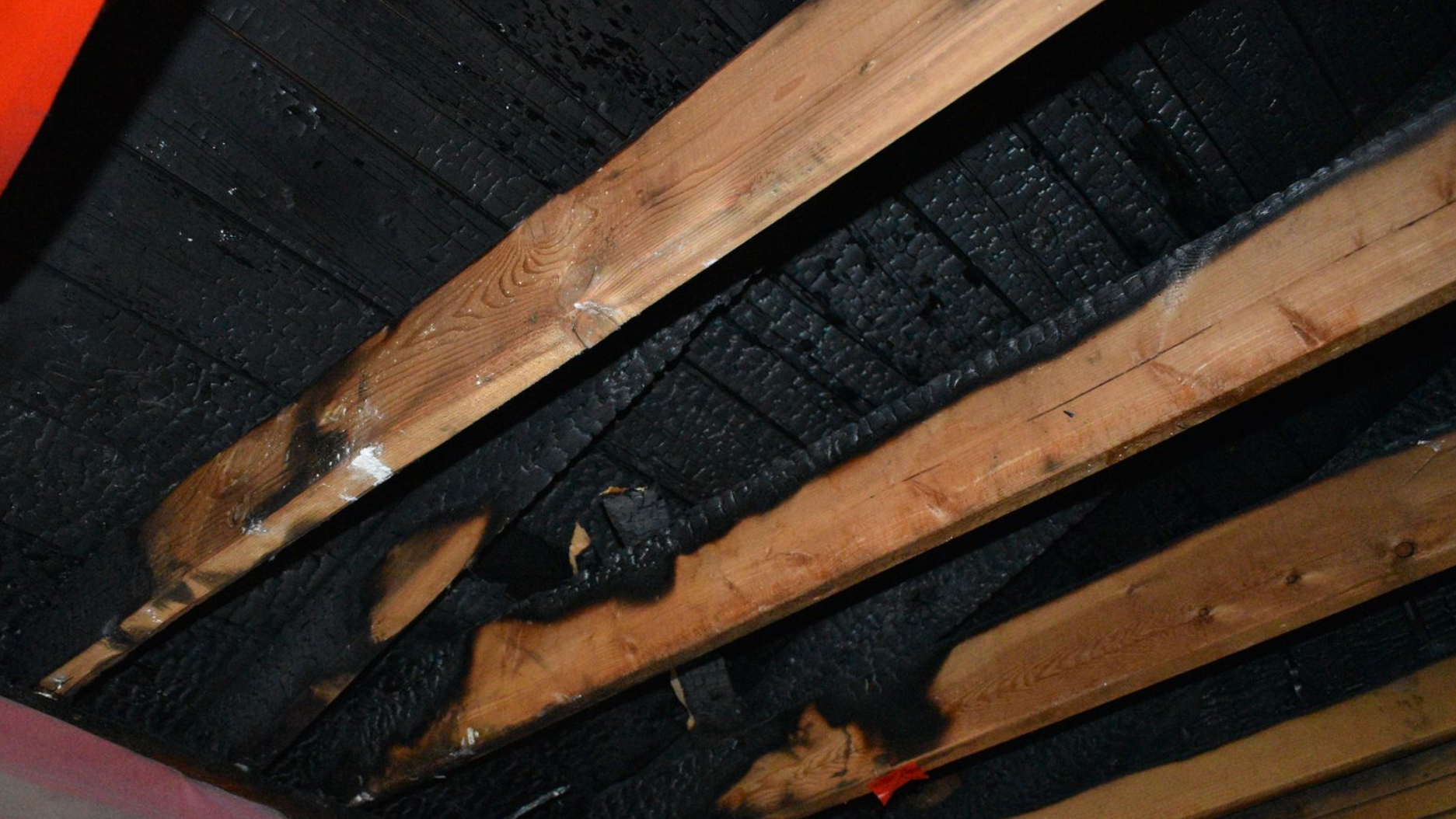 Burned wooden roof beams with charred black ceiling and smoke damage