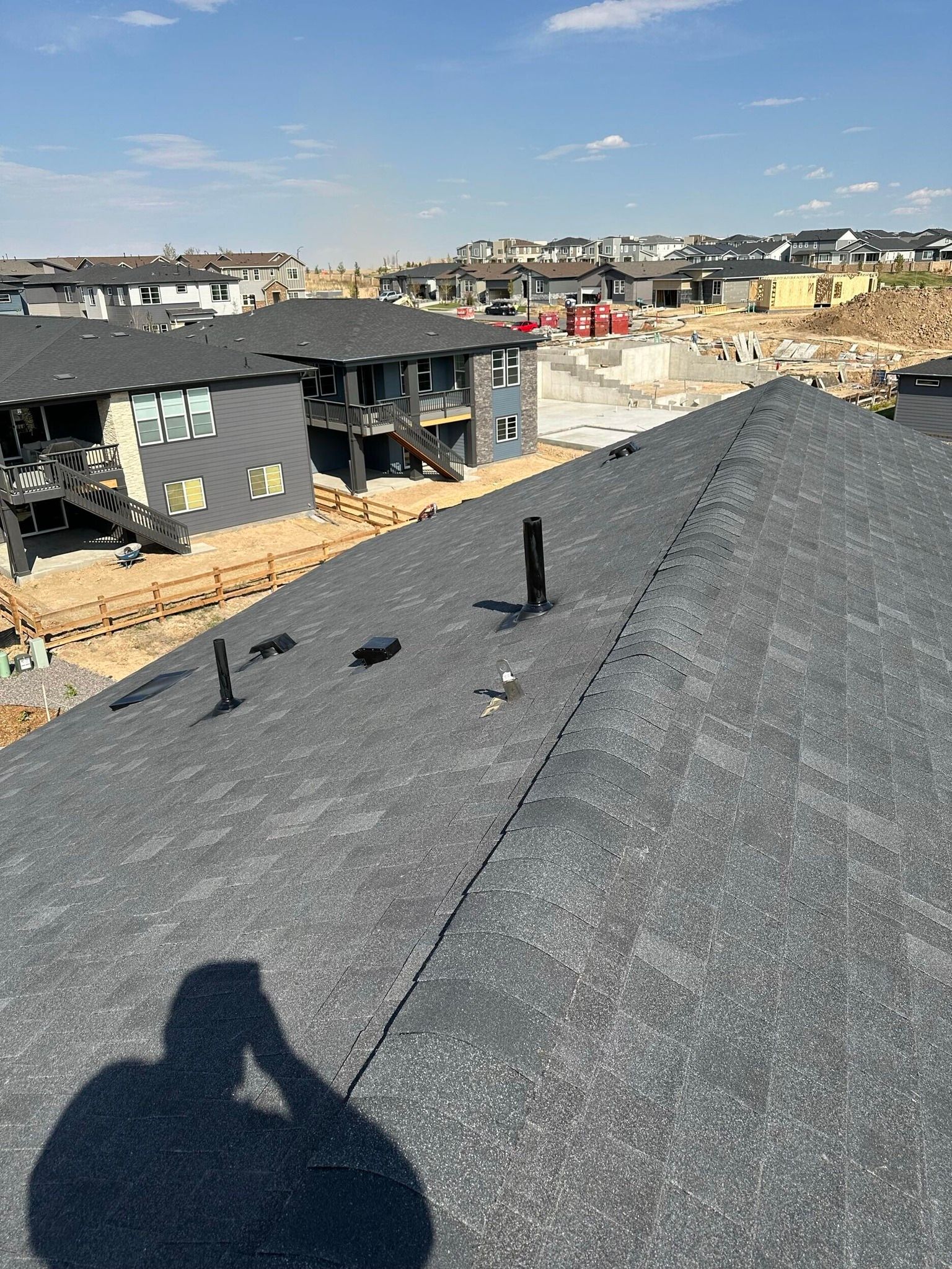 View from a shingled rooftop overlooking a suburban neighborhood under construction on a clear day