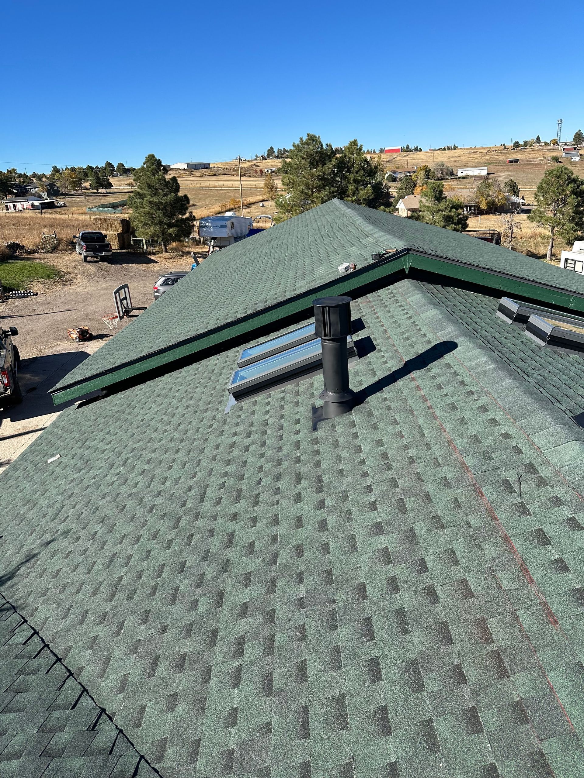 Green shingled roof with vent pipe overlooking a dry suburban landscape under a clear sky