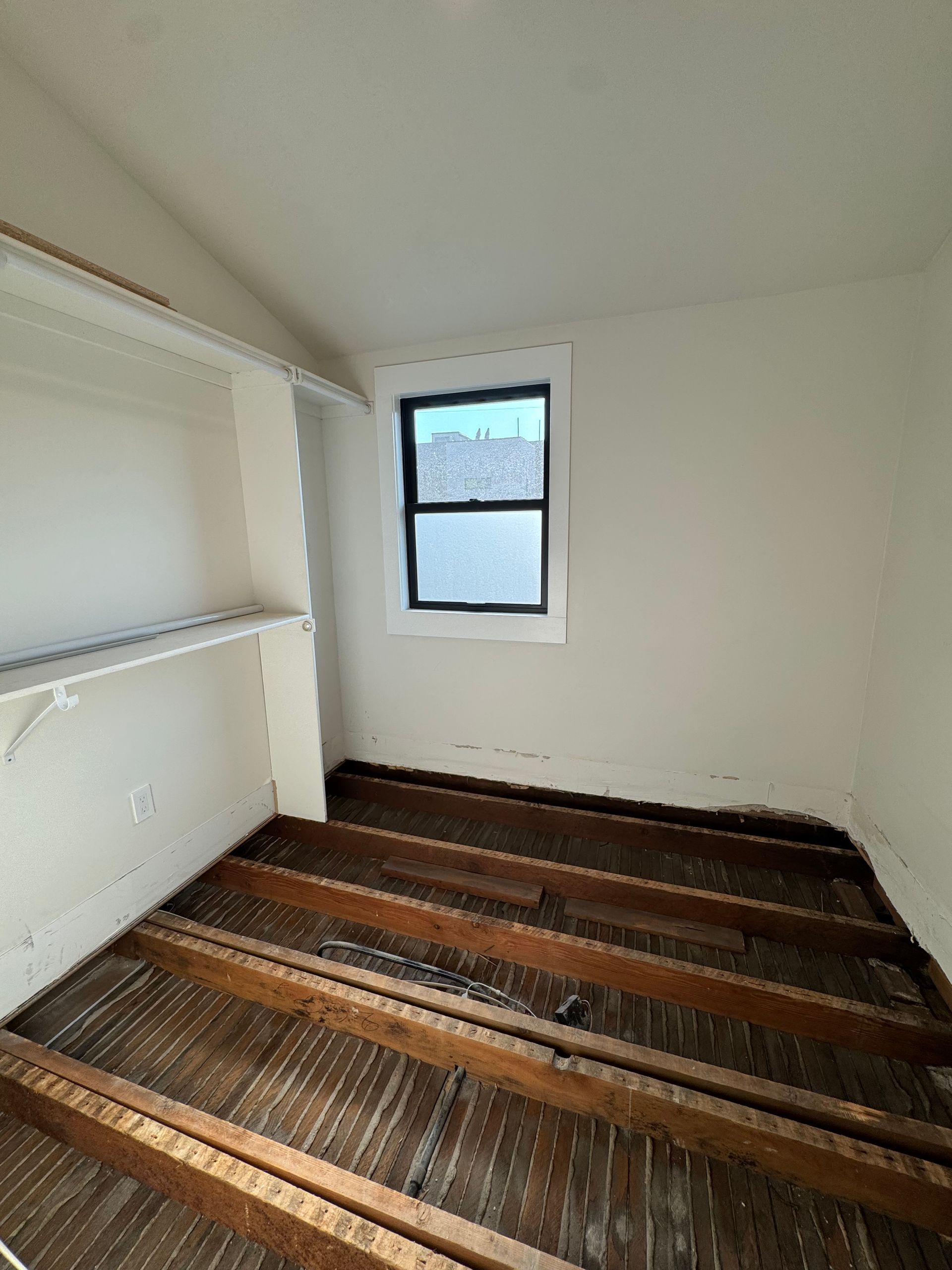 Empty small room with white walls, built-in shelf, window, and worn striped carpet flooring