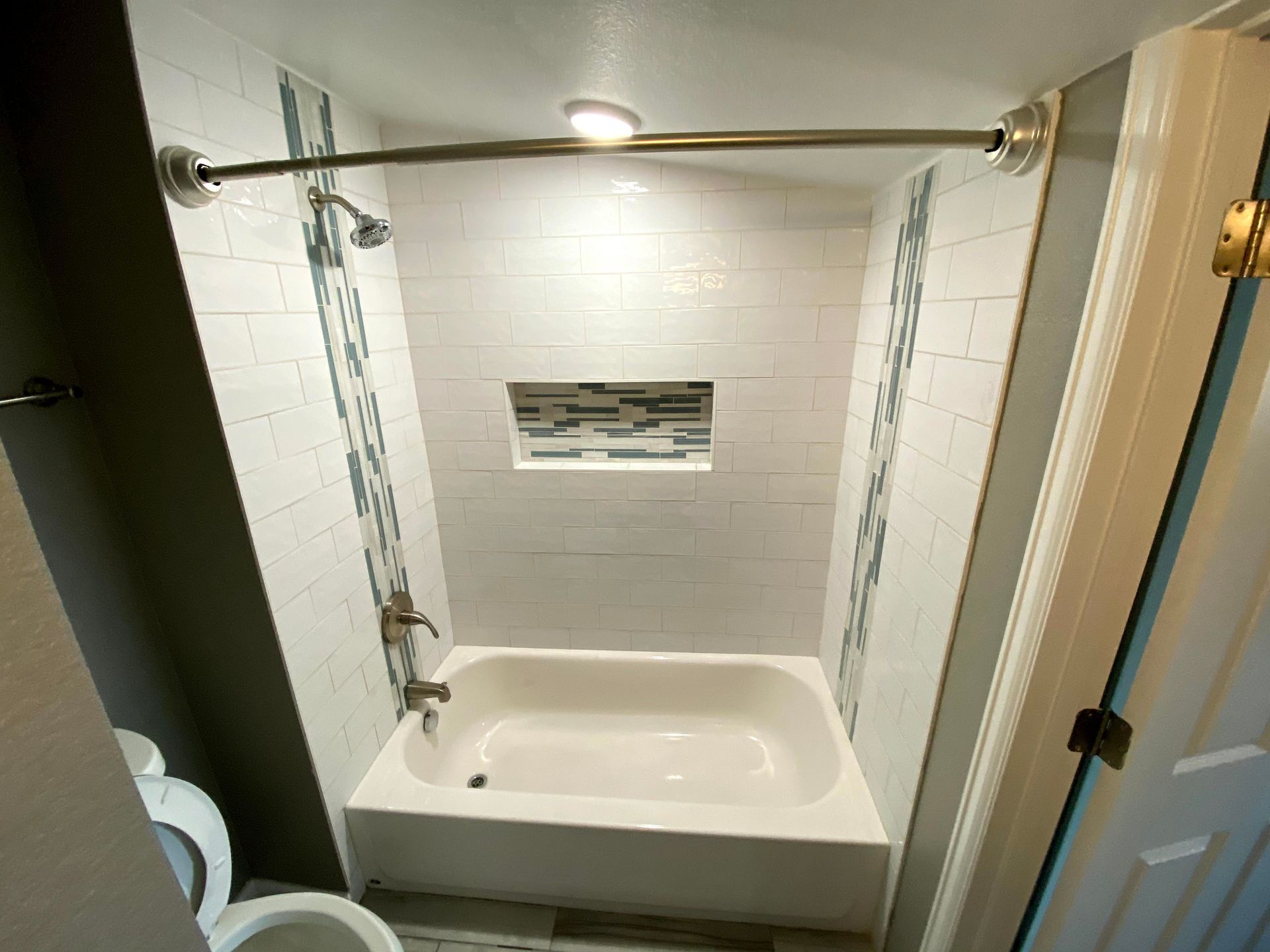 Small white bathtub in a tiled shower alcove with chrome curtain rod and grab bars