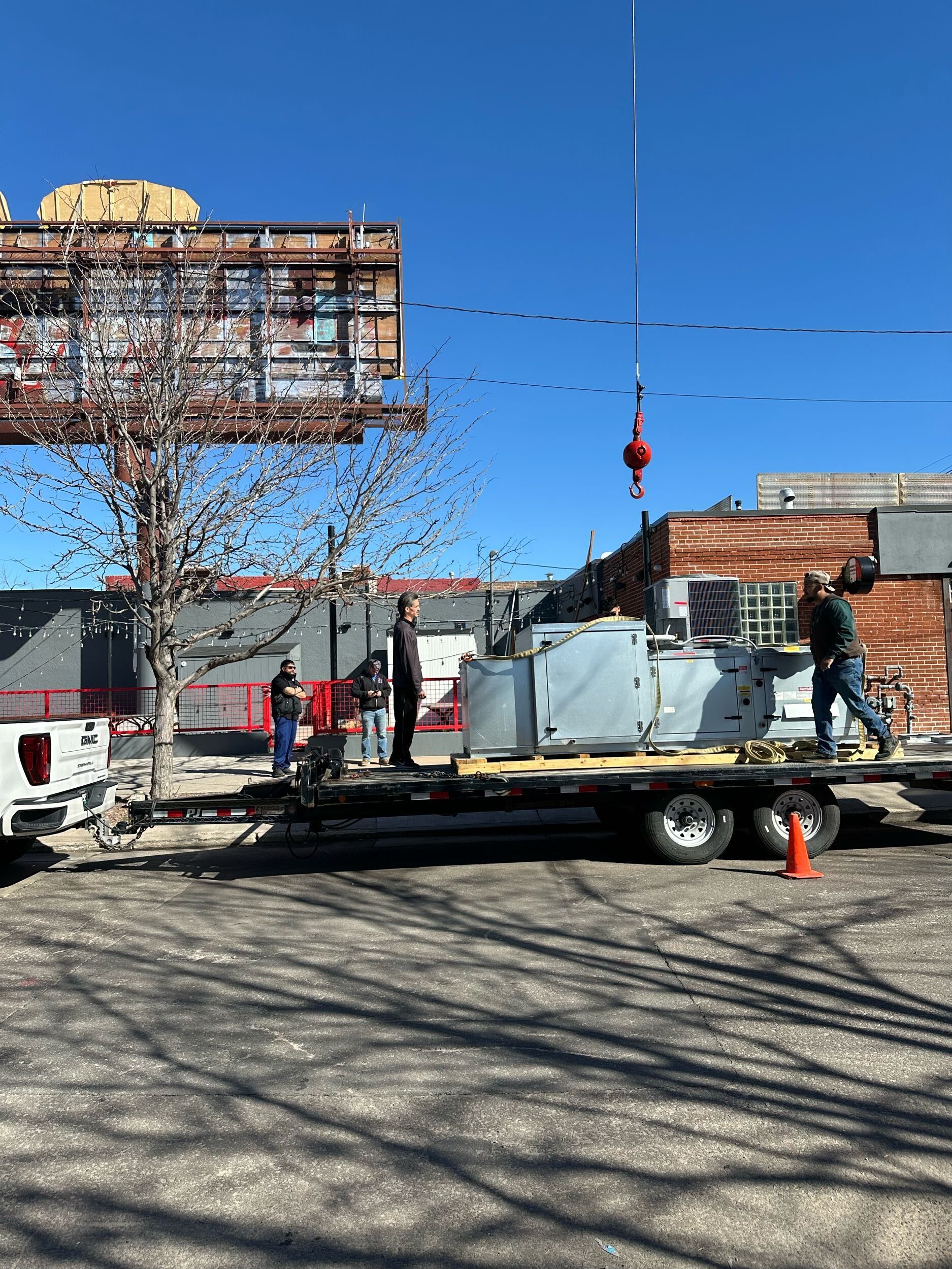 Flatbed truck with construction materials and workers on a street under a clear blue sky.
