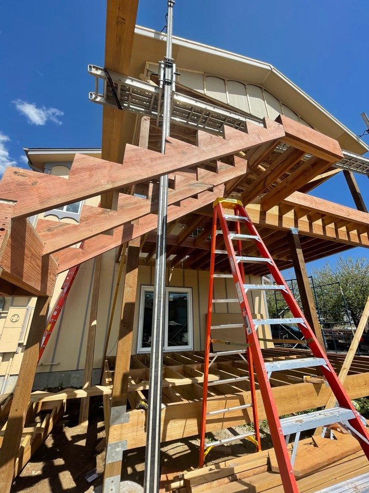 Worker on ladder installing wooden roof rafters on a house under construction.