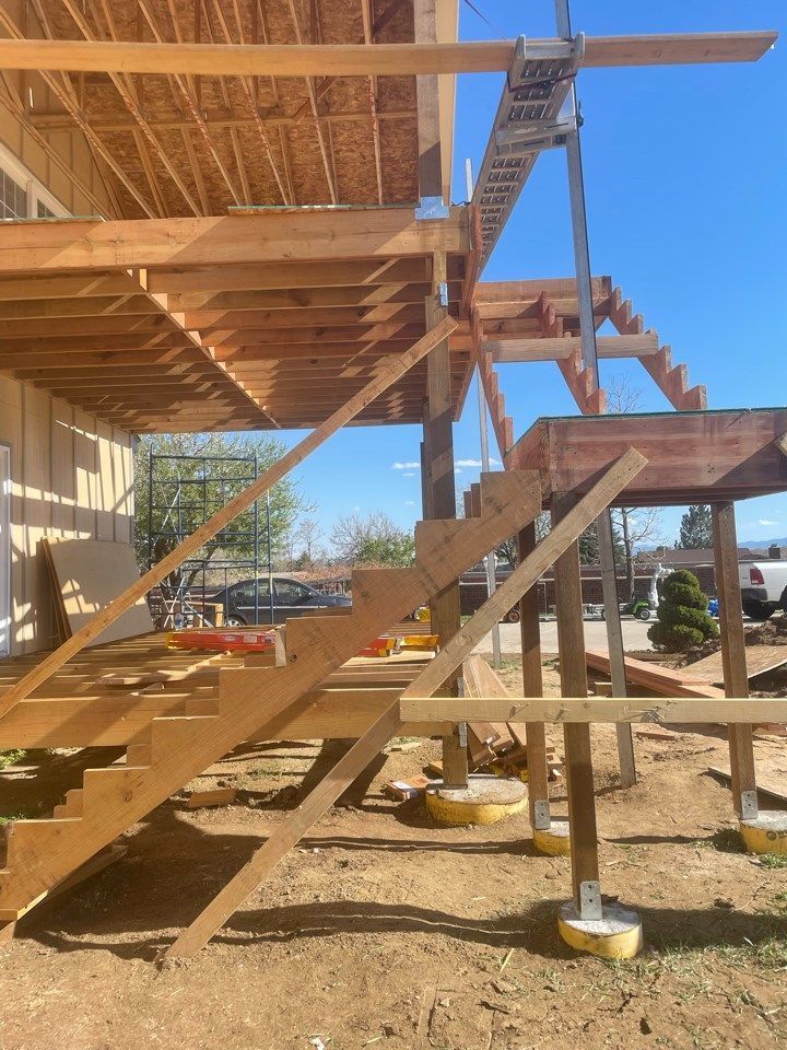 Wooden staircase under construction with metal supports and concrete footings beside a house