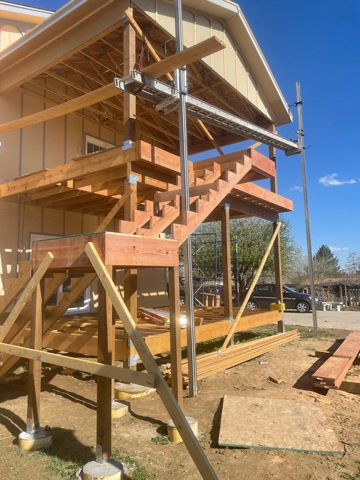 Wooden house under construction with exterior stairs and scaffolding on a sunny day