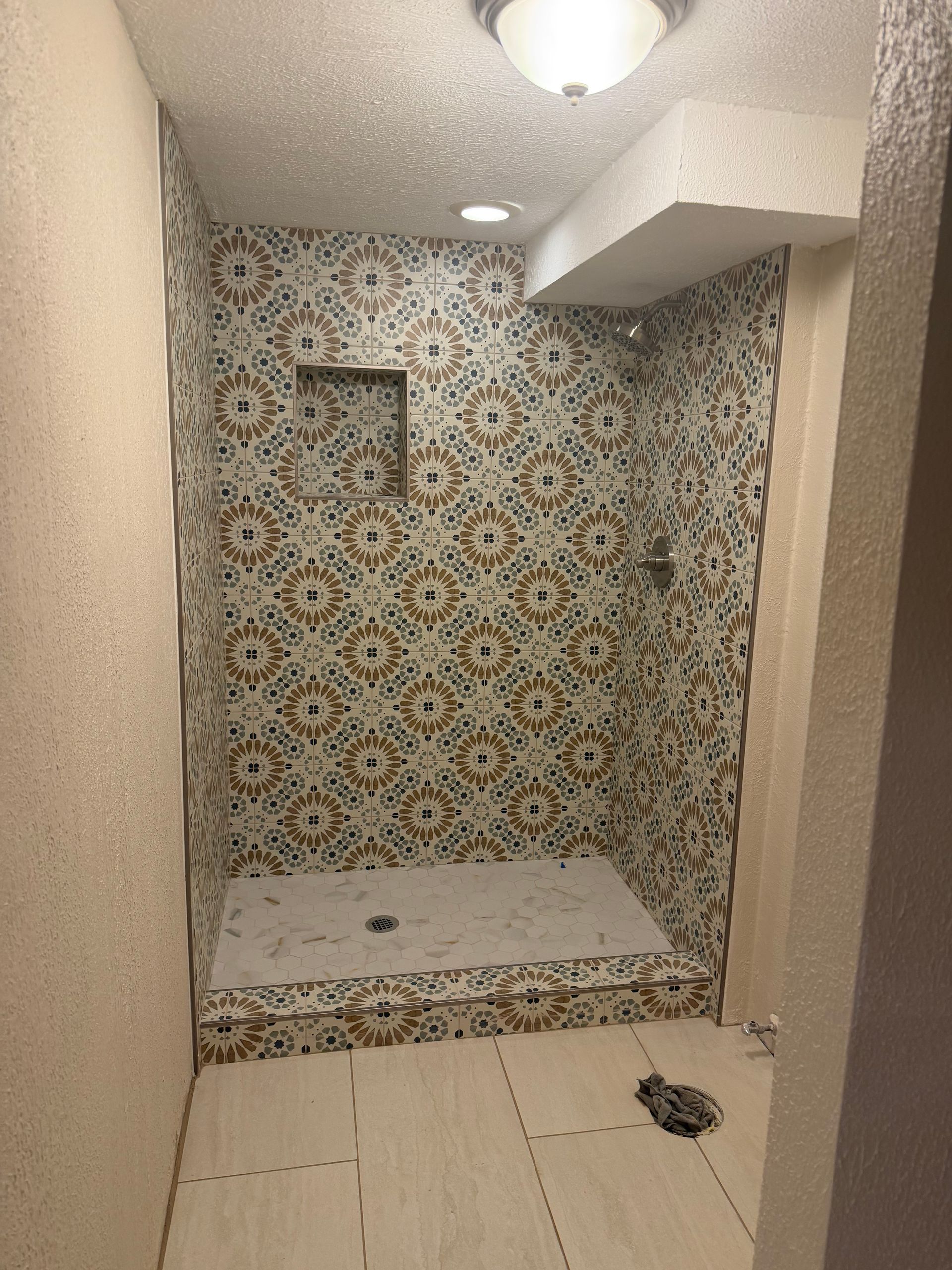 Small tiled shower nook with patterned accent wall, built-in bench, and recessed light.