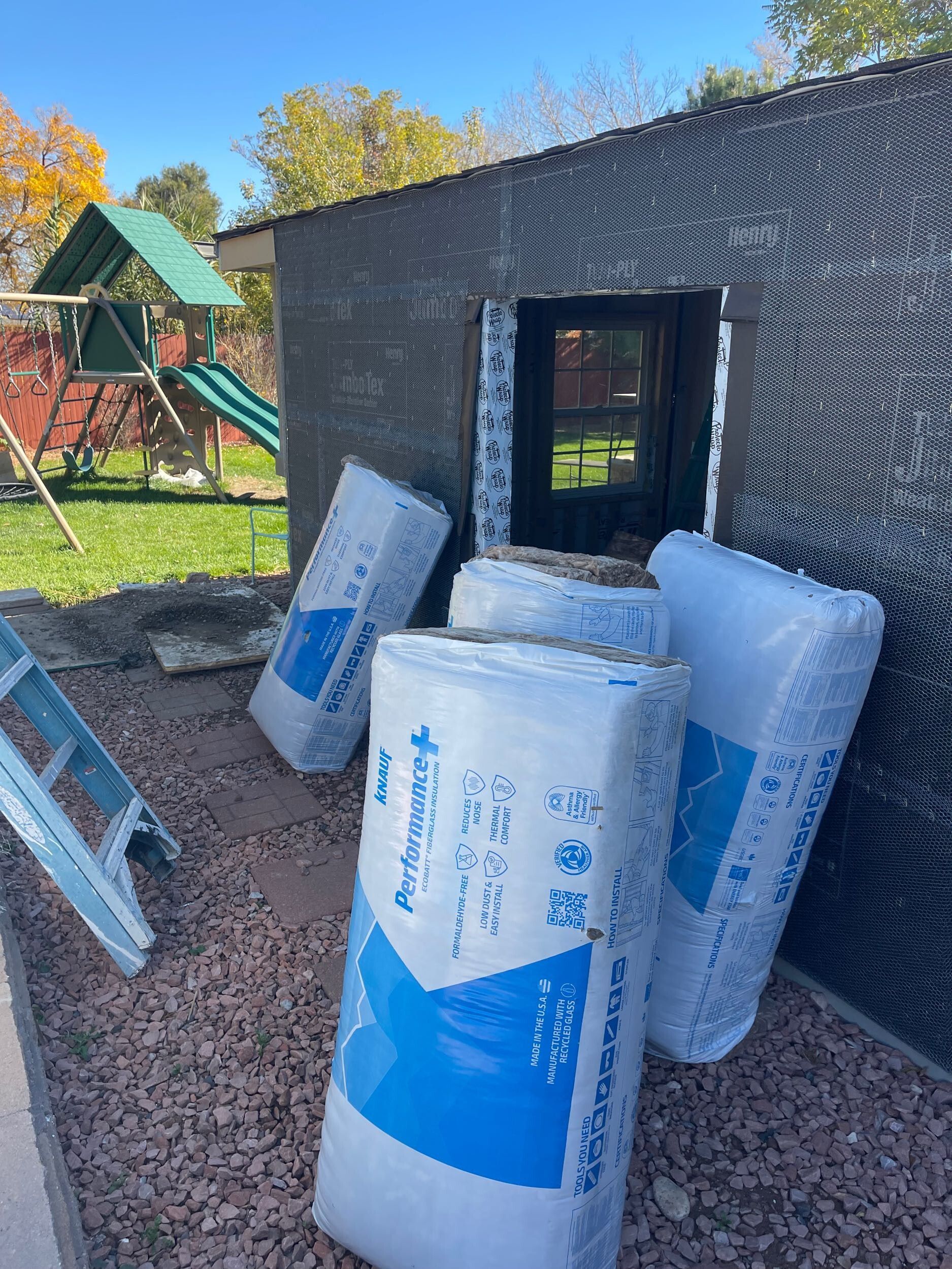 Foam insulation rolls stacked outside a partially built structure with a window opening