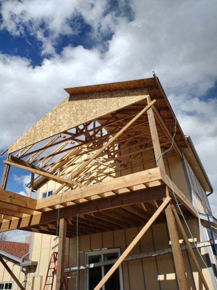 House under construction with exposed wooden framing and roof sheathing against a cloudy sky