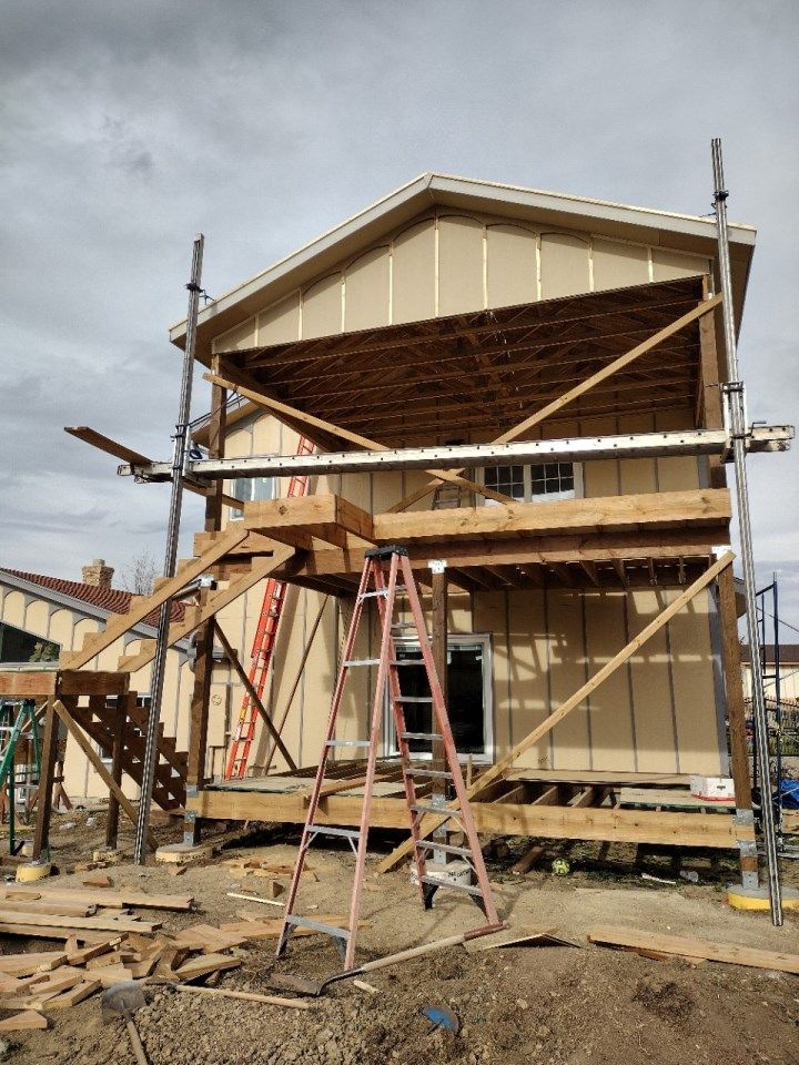 House under construction with scaffolding and ladders on a cloudy day