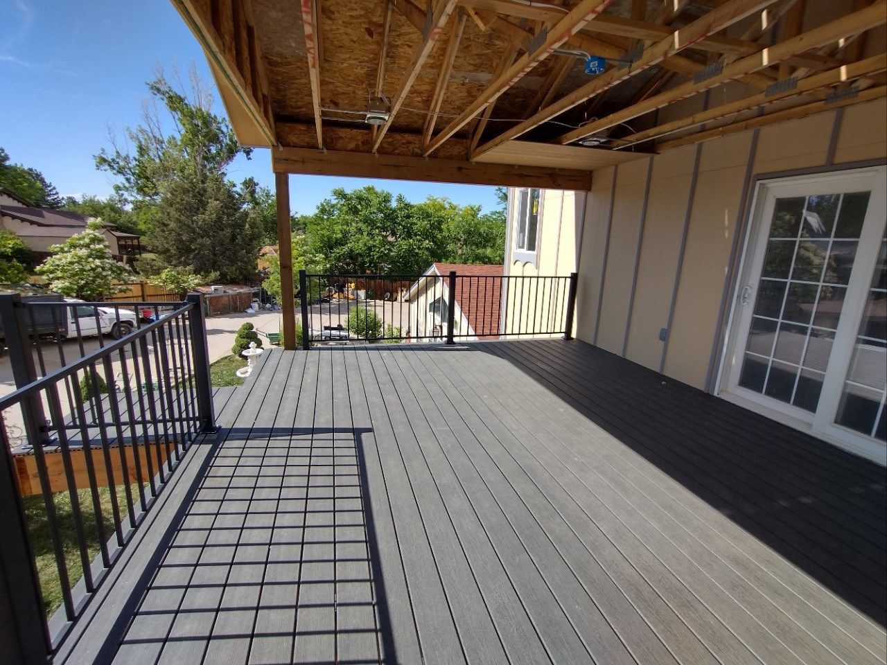 Covered wooden deck with black railing and sliding glass doors under construction