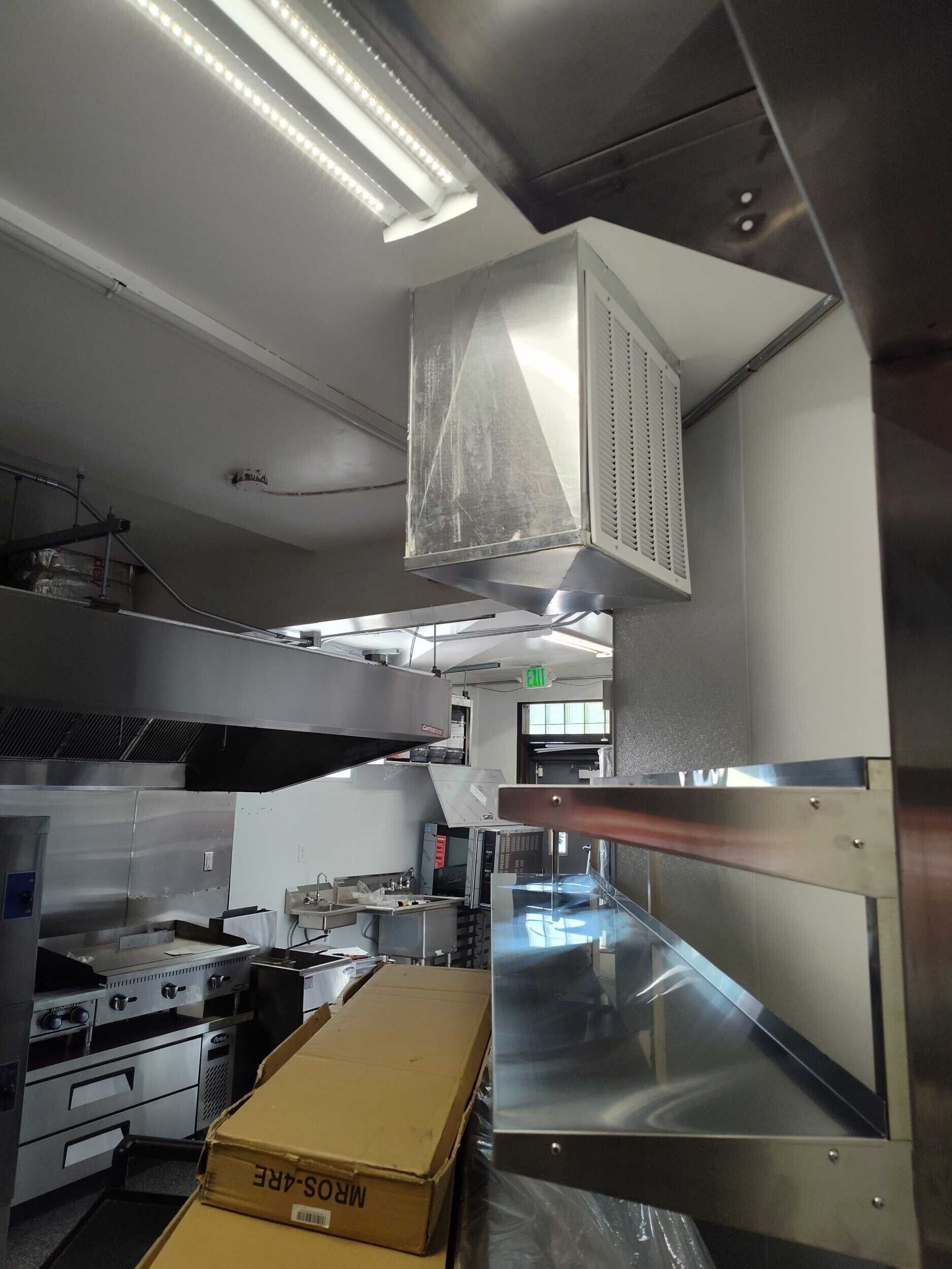 Commercial kitchen with stainless steel equipment, prep tables, and a cardboard box on the counter.