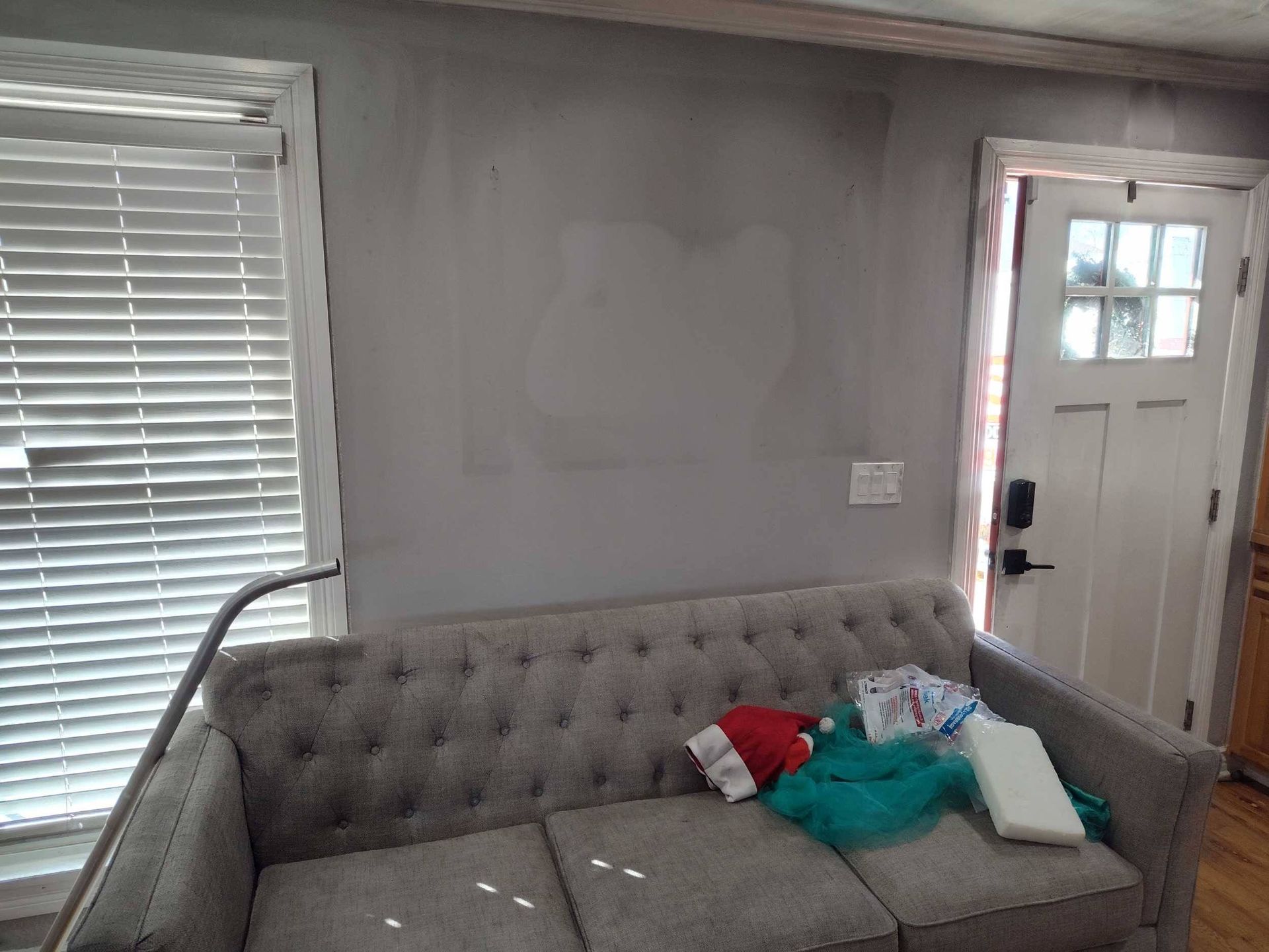 Living room with gray tufted sofa, pillows, and a front door in the background.
