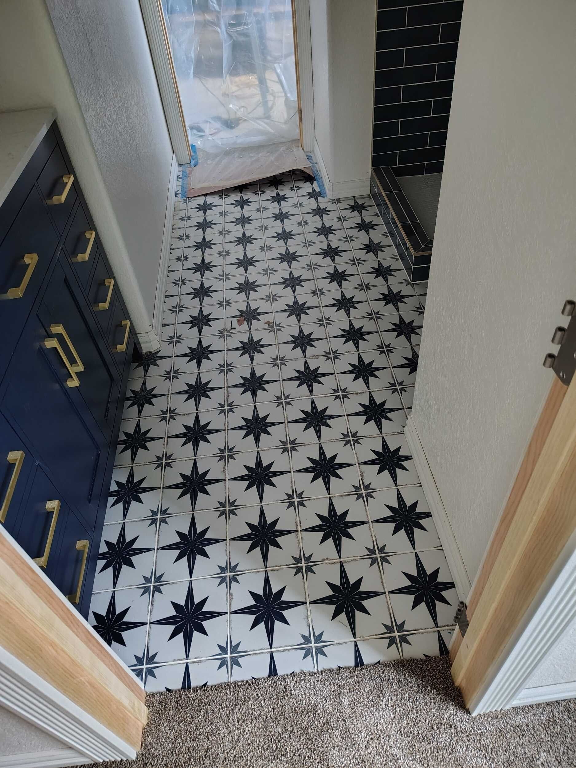 Narrow hallway with black-and-white patterned tile floor, blue cabinets on one side, and a doorway at the end.