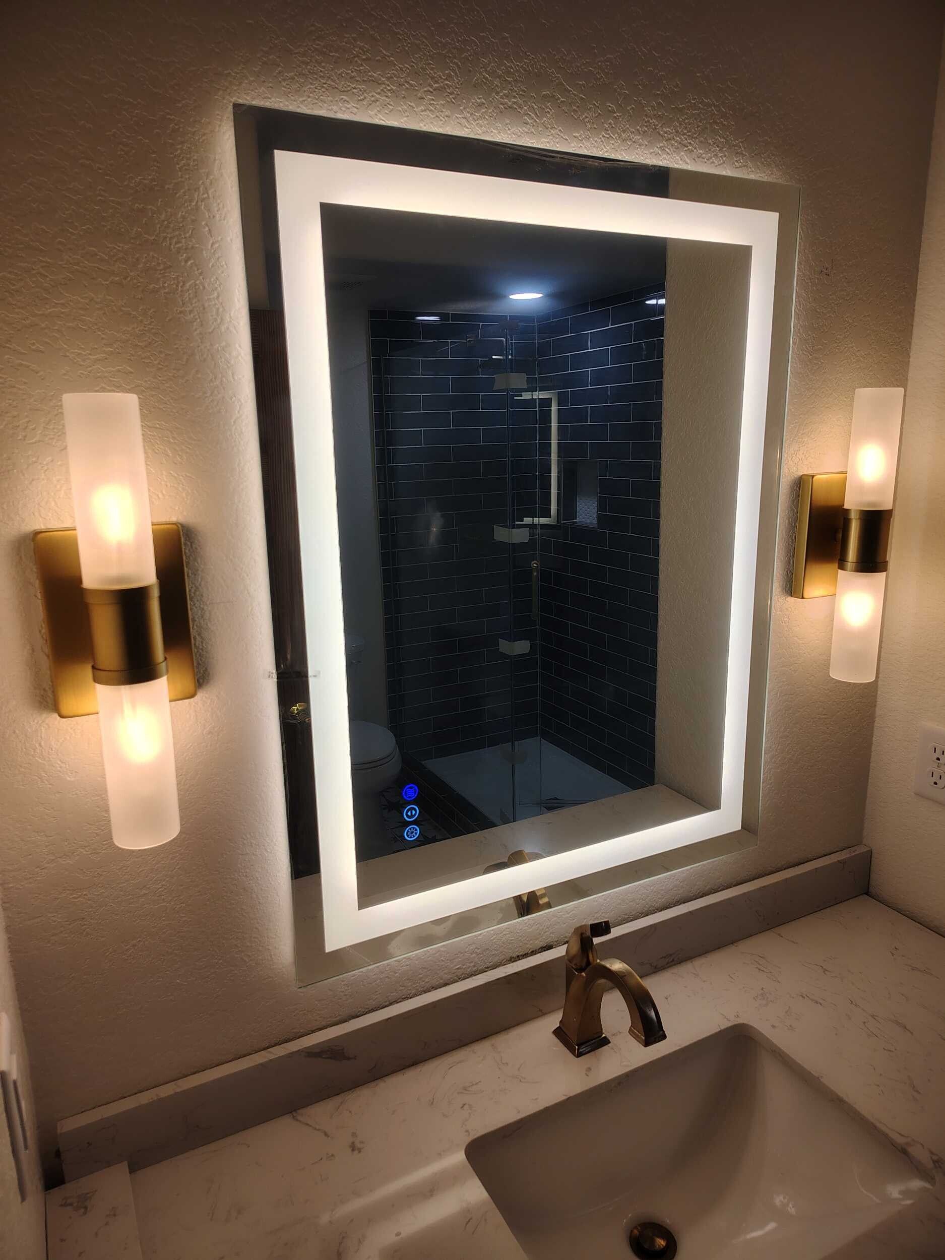 Bathroom vanity with illuminated mirror, sink, and wall sconces reflecting a dark window.