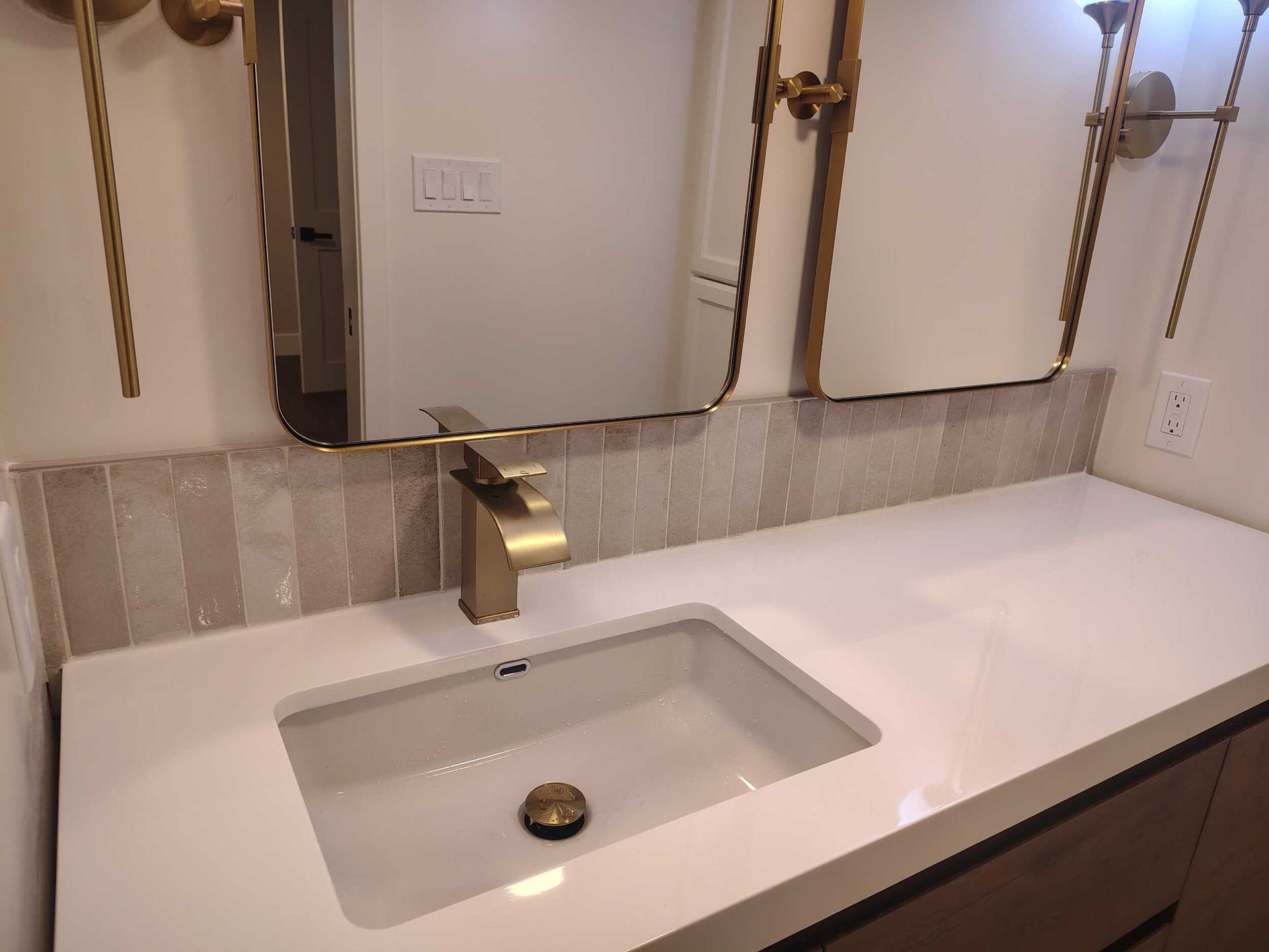 Bathroom vanity with white countertop, gold faucet, and rectangular undermount sink in front of framed mirrors.