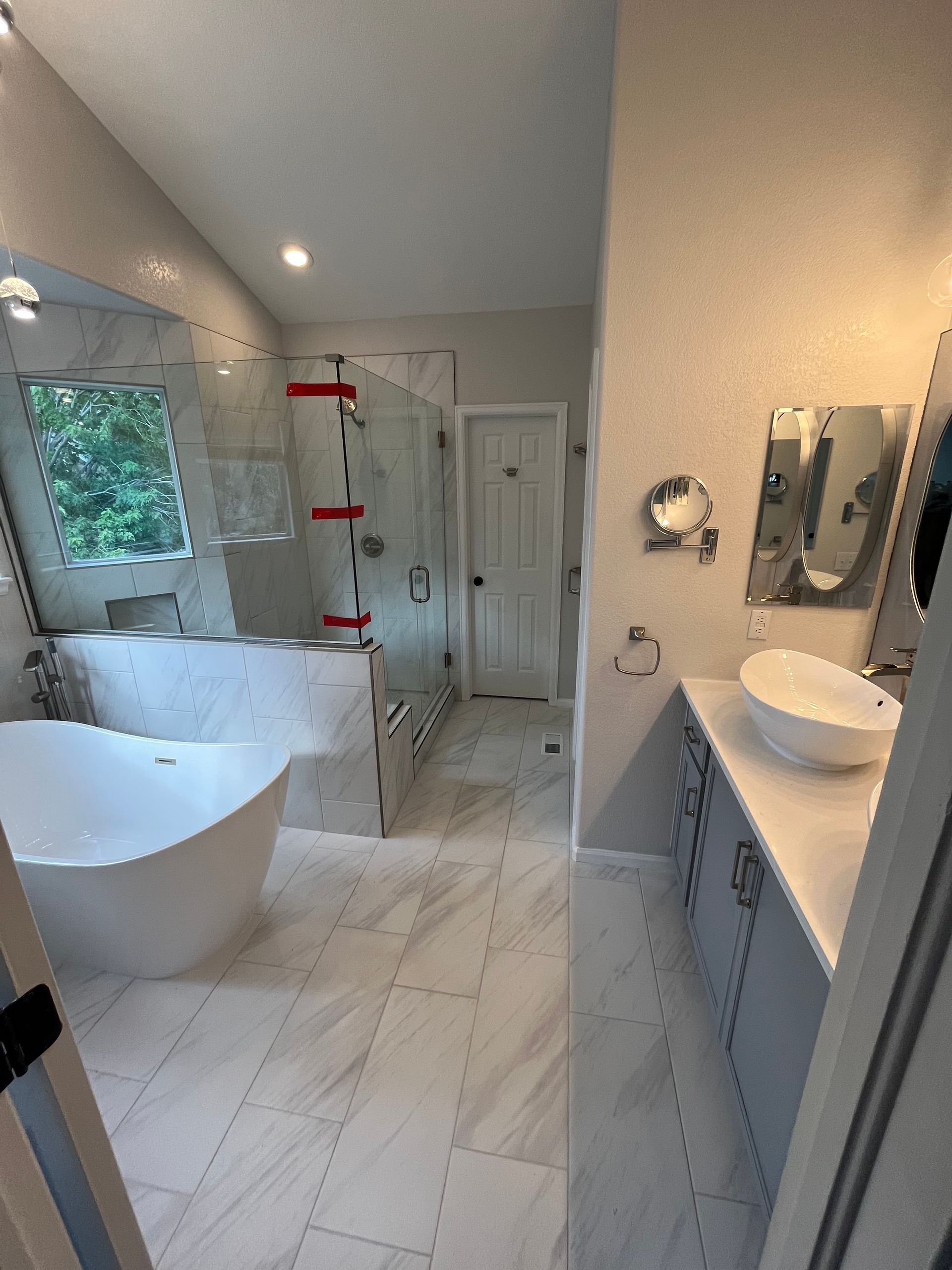 Bright modern bathroom with freestanding tub, walk-in shower, double vanity, and white marble tile.