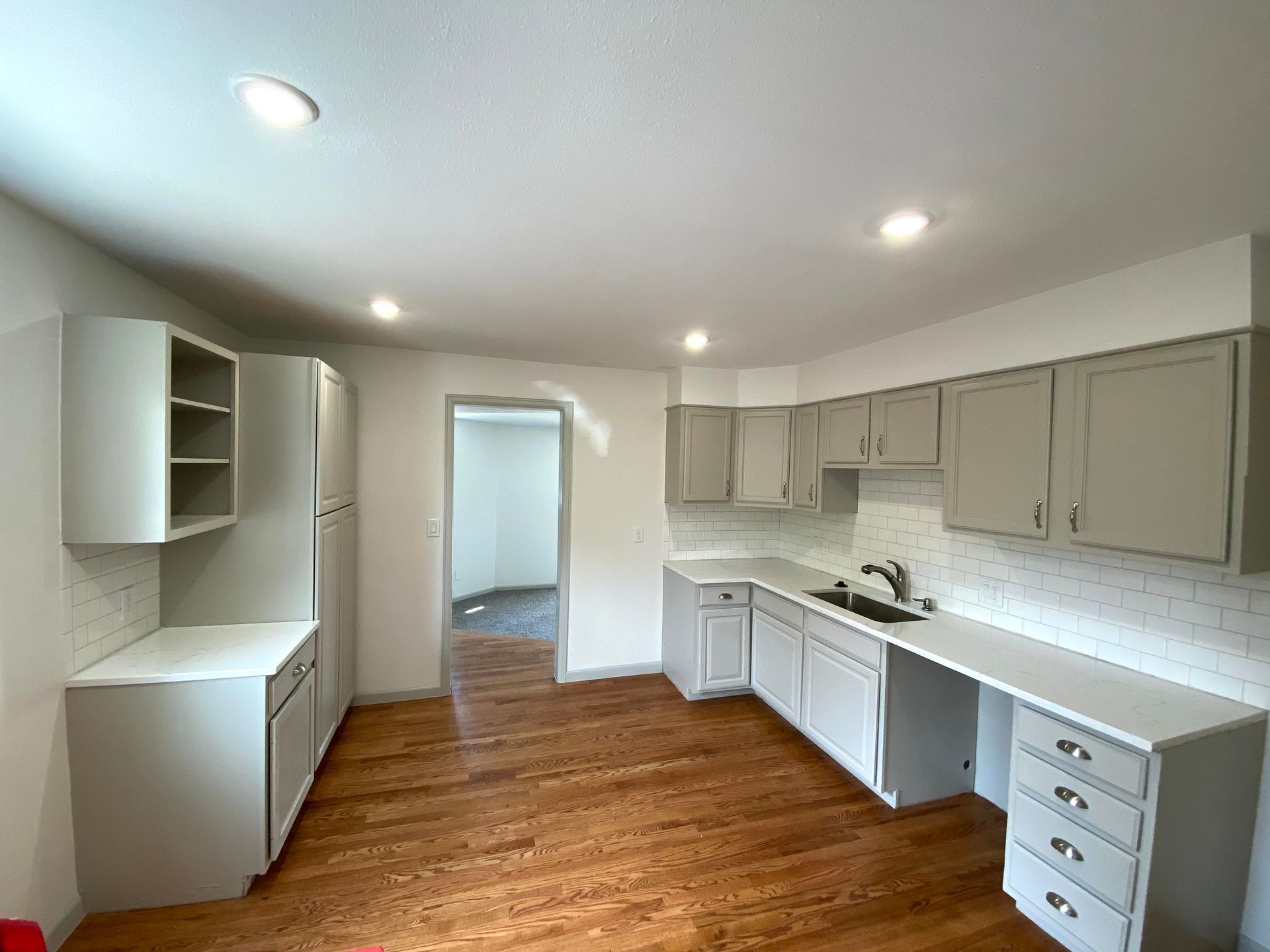 Empty modern kitchen with white cabinets, wood floors, and recessed ceiling lights