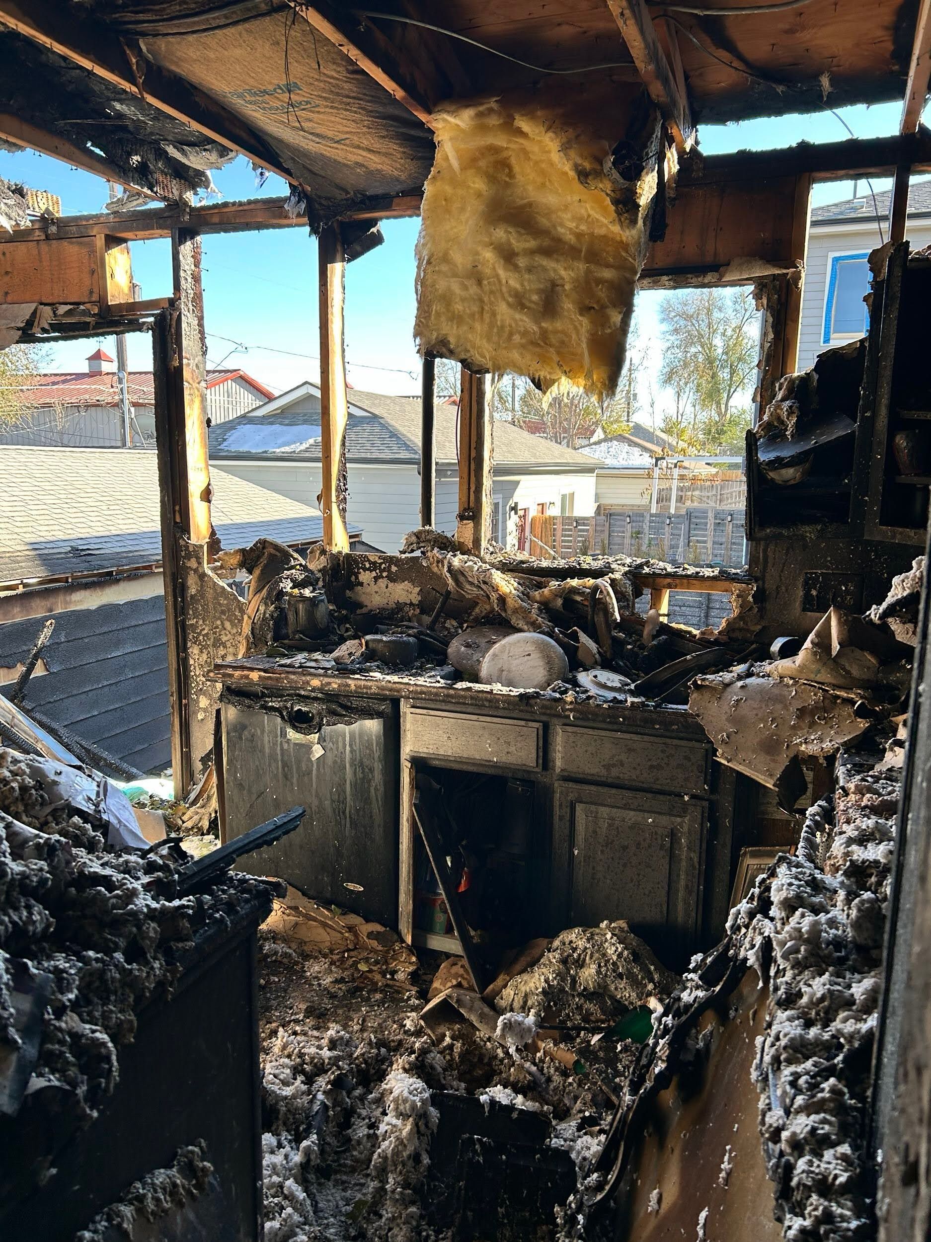 Burned-out kitchen interior with charred debris, a damaged counter, and a partially collapsed roof.