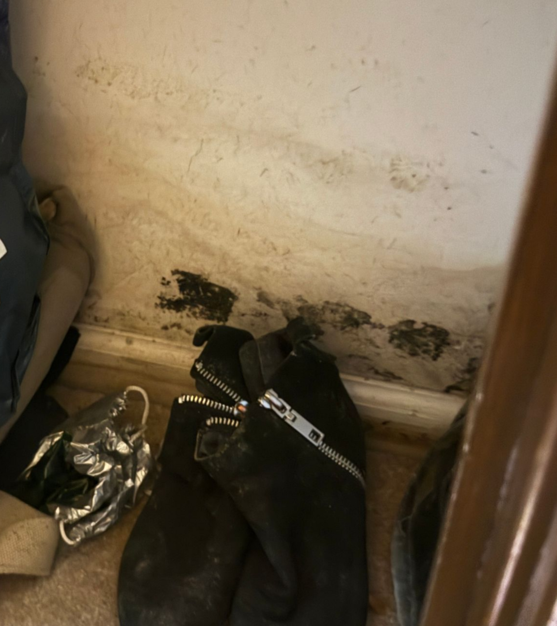 Black boots and silver shoes on a floor beside a scuffed wall with dark stains.