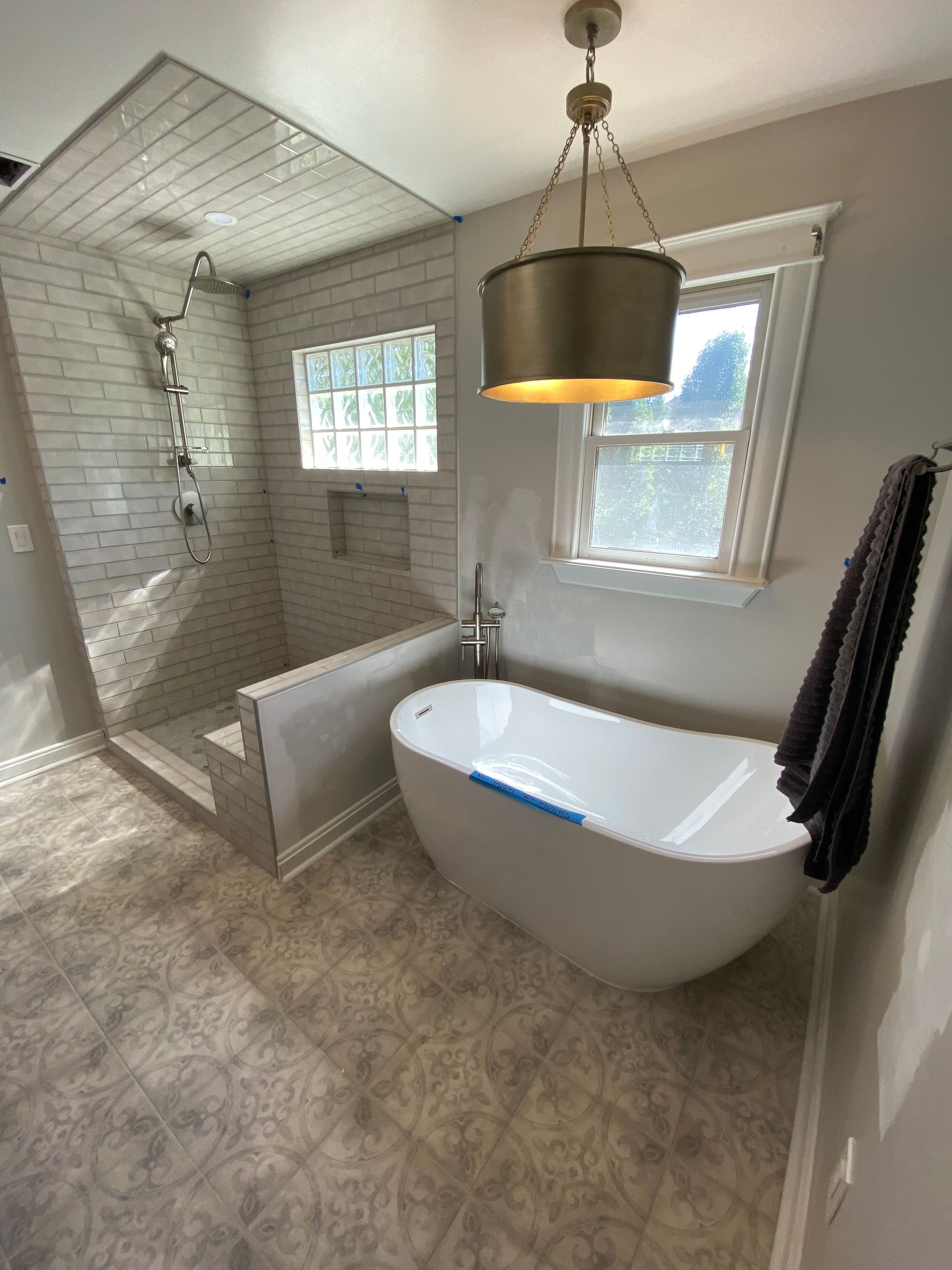 Bright bathroom with freestanding tub, tiled shower, window, and gray floor tiles.