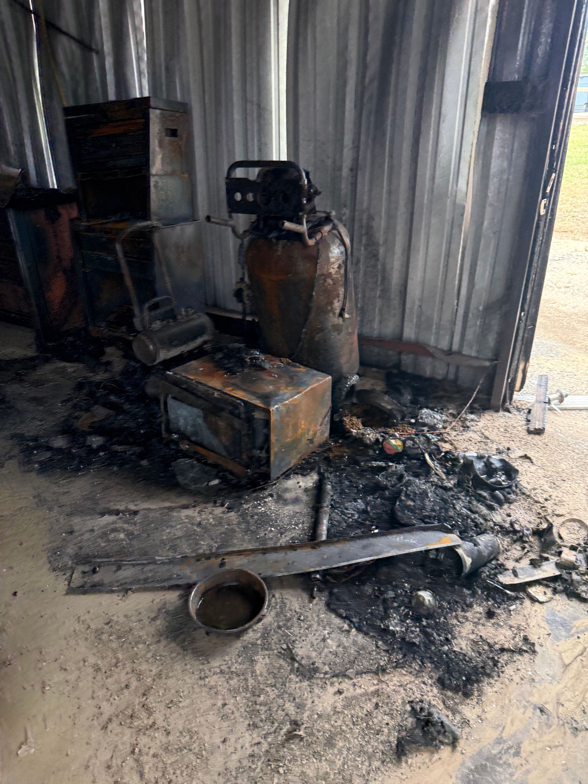 Burned room with charred debris, damaged machinery, and smoke stains on the floor and walls