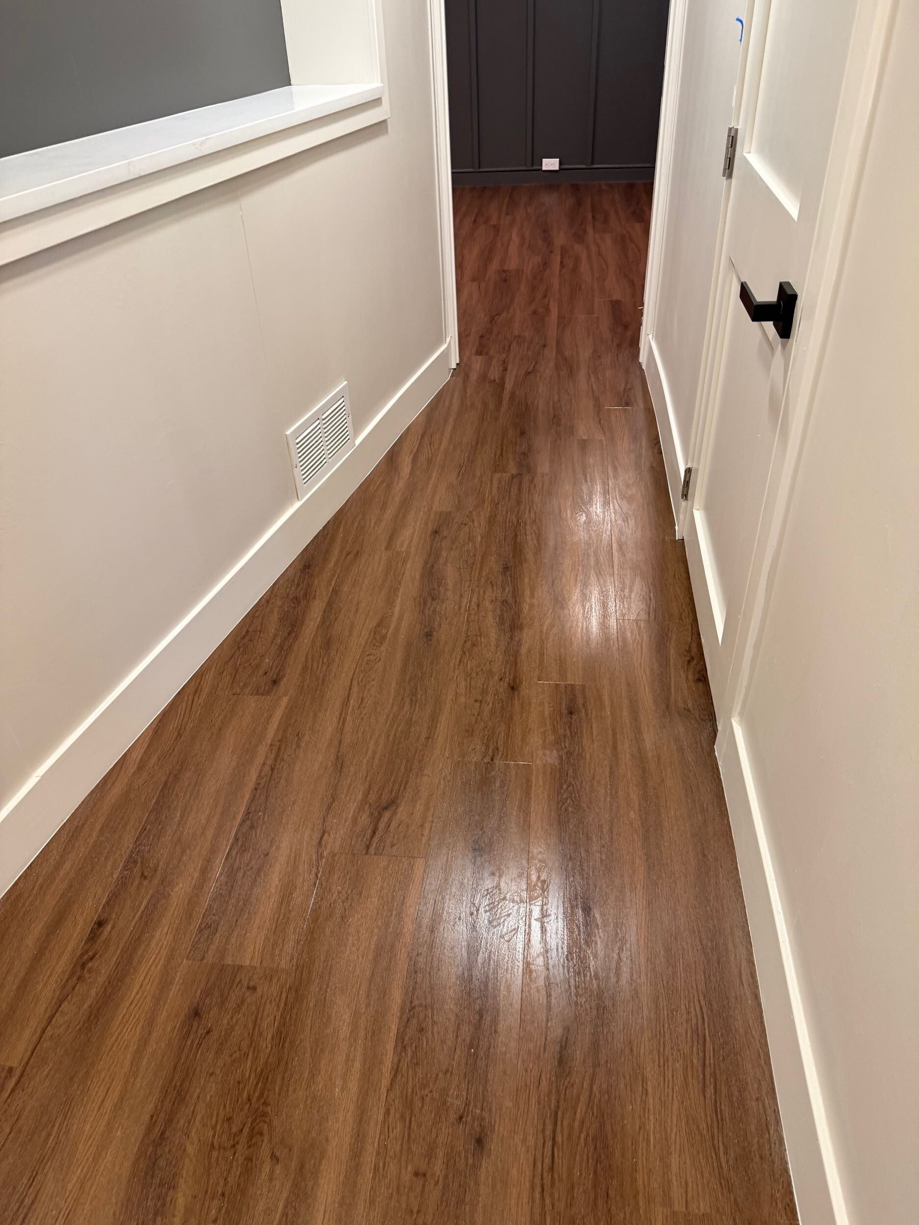 Narrow hallway with wood flooring, white walls, and a dark cabinet at the end