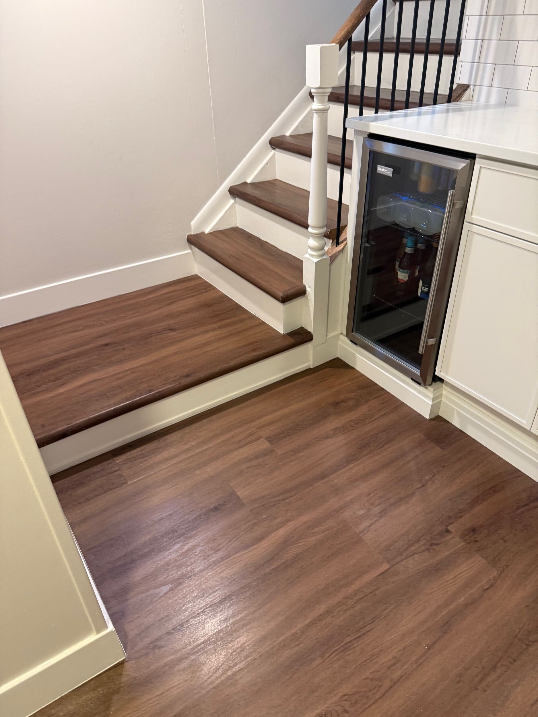Wood-floored interior with a stair step, white cabinetry, and a glass-front appliance or display cabinet.