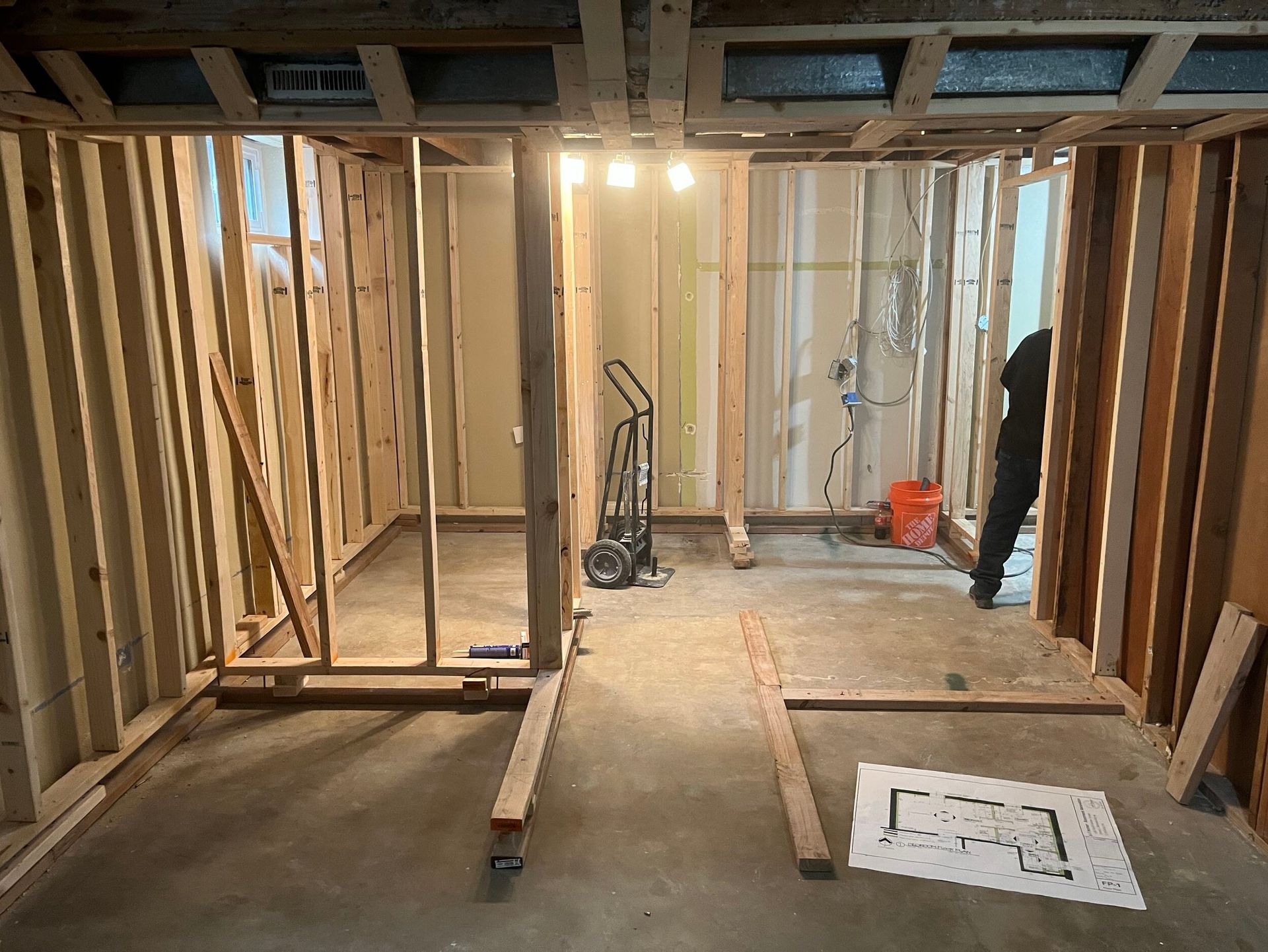 Basement under renovation with exposed framing, a shop vac, and unfinished floor markings.