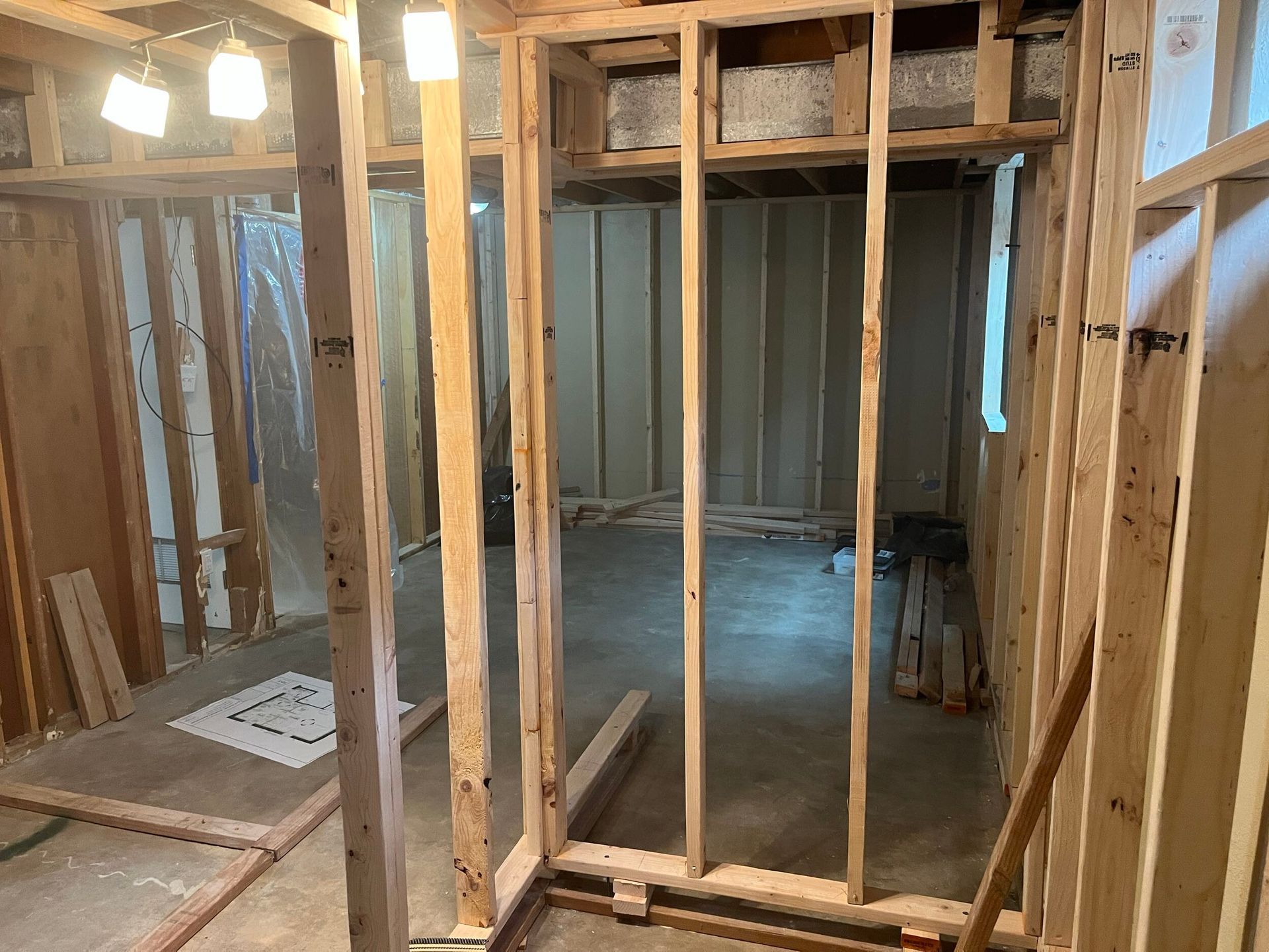 Unfinished room with exposed wood framing, hanging lights, and a doorway opening to a dim hallway.