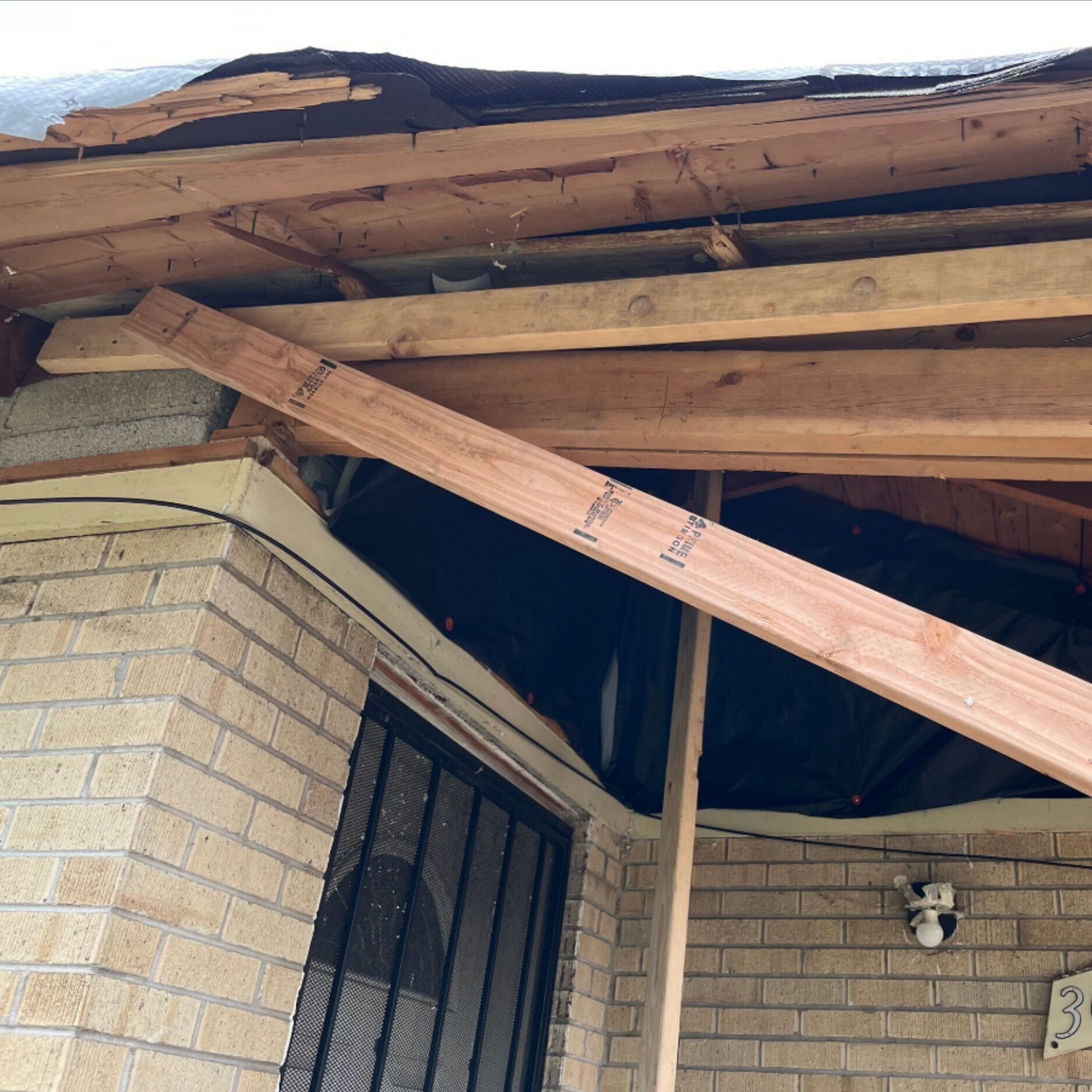 Broken roof beams above a brick porch with exposed rafters and a diagonal support plank