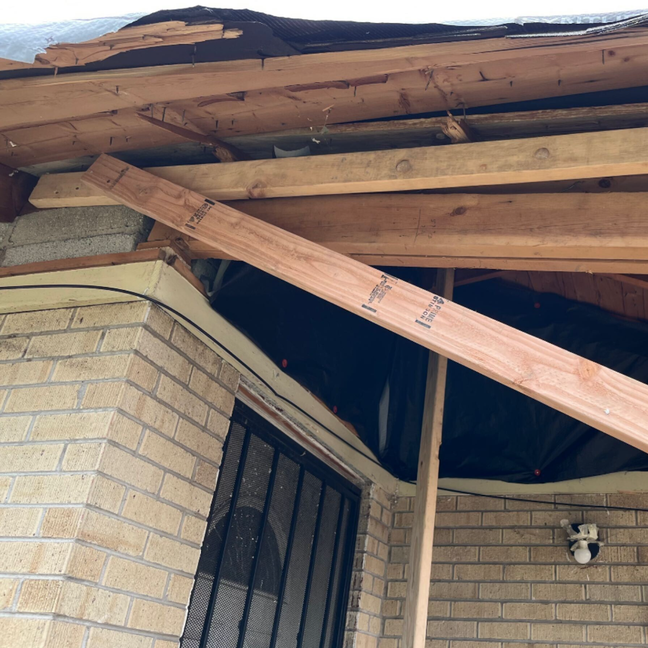Damaged house roof with broken wooden beams over a tan brick wall and window