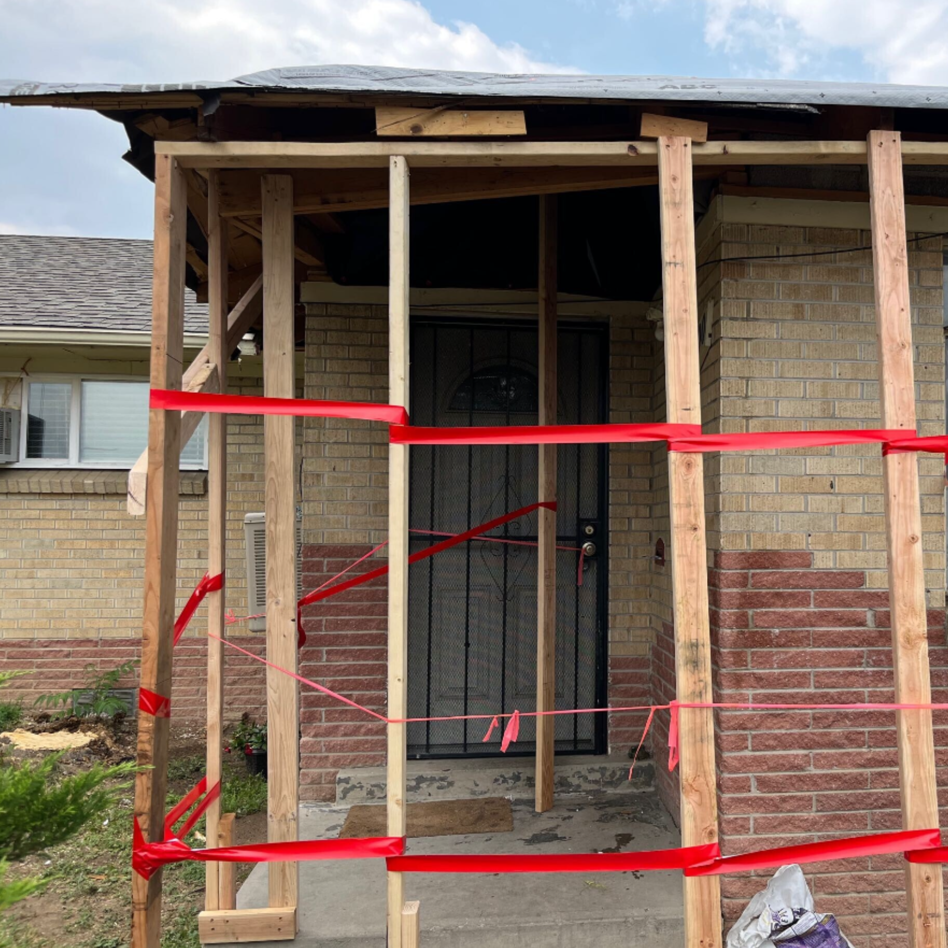 Front porch under construction, with wooden framing and red safety tape in front of a brick house.