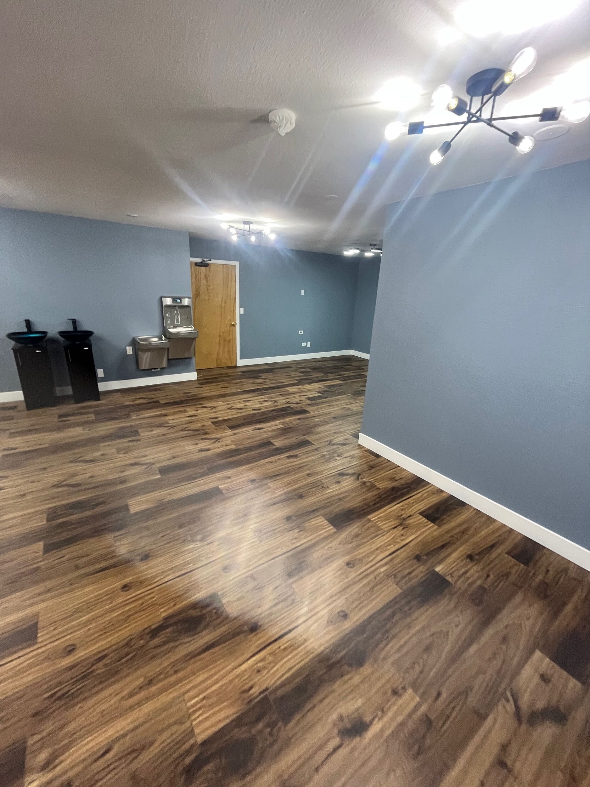 Empty living room with blue walls, dark wood floors, and a ceiling fan-light fixture